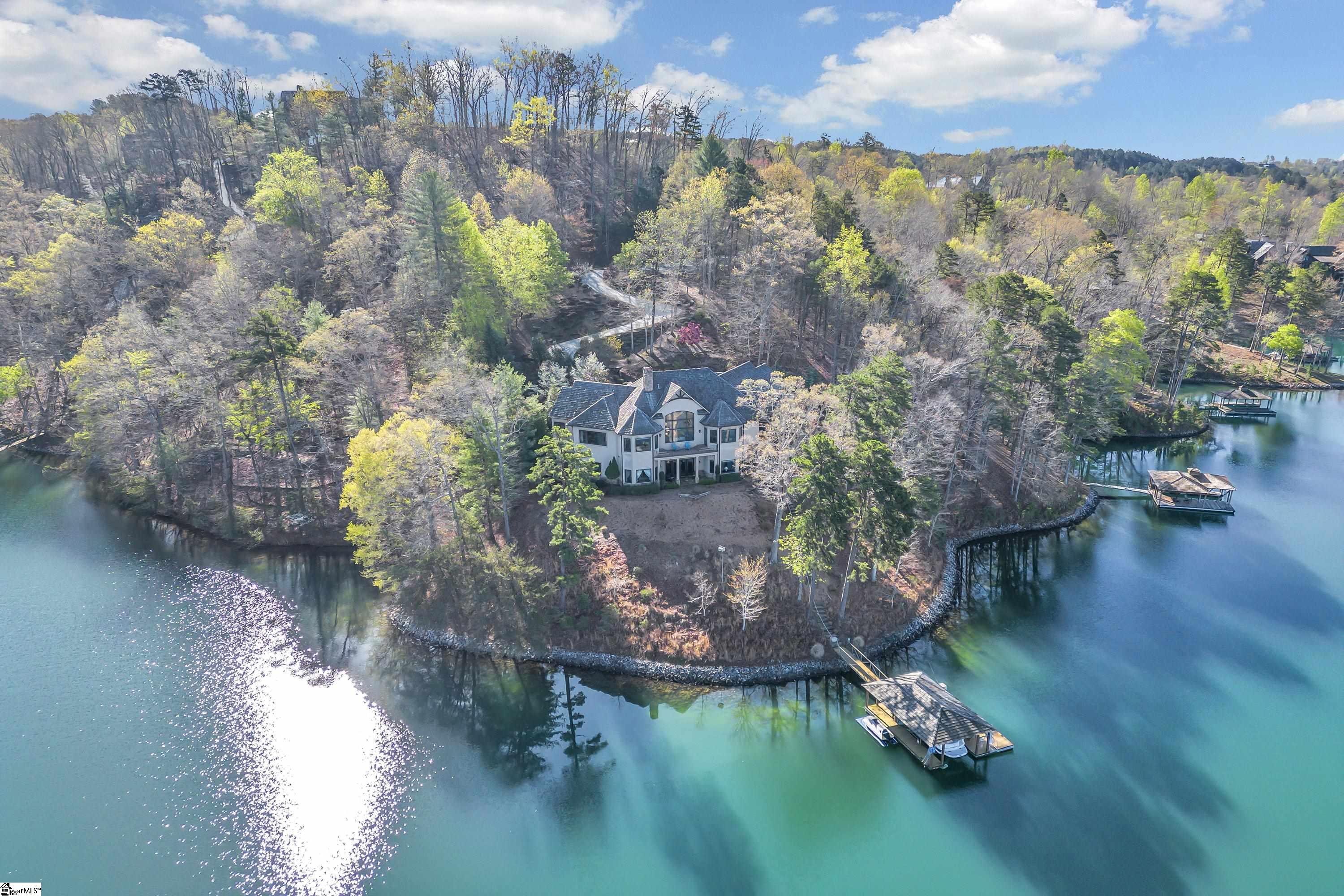 Located on an incredible point lot, 117 Misty Water Loop offers expansive and enviable views of serene open water. The front entrance with its commanding double doors gives the feel of a grand mountain lodge while striking turrets facing Lake Keowee are reminiscent of the European countryside. This home’s story is one of shape and texture as architectural details elevate both the exterior and interior spaces. With the distant Blue Ridge Mountains providing a wondrous backdrop, it is surrounded by idyllic landscaping.  Inside, a soft archway welcomes you to a vast open area where the big water itself is naturally part of the ambiance. The great room is anchored by a stone fireplace and has a built-in entertainment center and shelves and a refined vaulted ceiling juxtaposed beautifully with rustic beams. Have your morning meal or beverage in a bed and breakfast setting as you soak in the scenery from the dining area or spacious bar. The kitchen is equipped with a double-door stainless KitchenAid refrigerator, a wine refrigerator, a double oven, a five-burner Dacor gas cooktop, a large island with its own sink, a new dishwasher, soft-closing drawers, a walk-in pantry, and pendant and recessed lighting.  Warm hardwoods draw you through the main floor where you’ll find a soothing study with built-in shelving, cabinets, and a credenza, along with another splendid perspective of the water. Also located on the main level, the master suite features a wonderfully spacious walk-in closet/dressing area with tasteful storage solutions that make organization simple. Among the amenities of the master bath are heated floors, a zero-threshold walk-in shower with body sprayers, an inviting tub, and custom cabinetry.  A sweeping, curved staircase adds an elegant touch of distinction, but you can also take the elevator to the lower level where there are three bedrooms, two full baths, and an immense recreation room with 12-foot ceilings, tile flooring, a fireplace, and a bar. This area has a personality of its own but fits the character of this gorgeous property. The lower level also has a climate-controlled 2,000-bottle wine cellar, a workshop with room to provide inspiration for any project, utilities including two water heaters, and storage.  The three-car garage has epoxy flooring, a 50-amp charging station for an electric car, and an unfinished area above it that could be converted from storage to living space. The driveway has been replaced with concrete and expanded. The washer and dryer are new, and there’s ample storage, along with countertops for sewing, gift-wrapping, or any task made less laborious by the large laundry room. Additional highlights include a central vacuum, a new generator that serves the entire house, speakers throughout the home, and Pella windows.  In addition to the plethora of interior options, you can enjoy thoughtfully designed exterior sites on both levels where the vistas are immersive. The screened-in porch has a fireplace, a covered area with doors for the TV, and a grilling deck. All the decking is maintenance-free Trex®. Lower-level patios and boulder steps make for easy access to 288 feet of perfectly finished, riprapped shoreline via a high-quality Ipe wood Reserve dock with a cedar shake roof. Don’t let too many sunsets pass without a view from Misty Water Loop. The Reserve features over $100 million in amenities, recently announced new additions will include 12 hole par 3 course, sporting clays, lighted range and putting green.  This property has Full Membership allowing buyer to purchase Premier, Sports or Social Membership at closing.