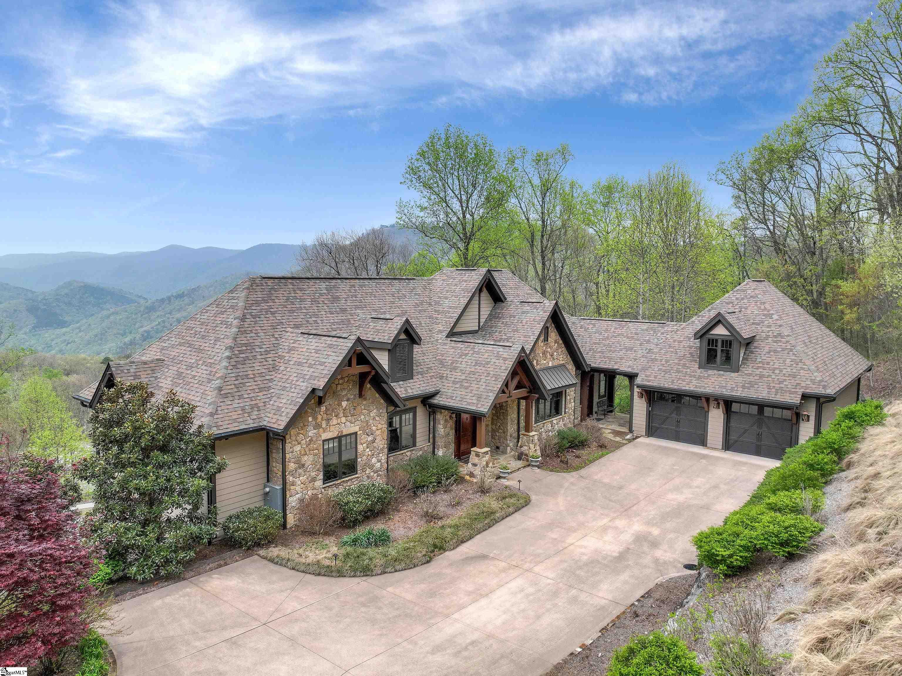 Nestled in the mountains just minutes from Greenville, SC, make yourself at home in the comfort and convenience of The Cliffs Valley gated golf and wellness community.   Ideally sited on 3.33 acres, this relaxing mountain home is rich in quality and design and features some of the most expansive, ridgeline vista views you’ll find in the Blue Ridge mountains.  Located at an elevation of 2,400 feet on a beautifully landscaped lot, the home features concrete composite siding and handsome stone exterior with a welcoming flagstone entry.    Entering the home, you are immediately captured by the impressive attention to detail in the elegant but rustic finishes.   The main level is laid out gracefully with the primary suite on one wing and an open floor design with the kitchen, dining area, and great room all combining seamlessly into a warm and welcoming space for entertaining guests. The great room is stunning with its stacked stone gas fireplace, cedar beams, cathedral ceiling, and an abundance of tall windows to allow an infusion of light throughout the day.  Adjacent to the dining area, the spacious cook’s kitchen is fully equipped with granite counters and a chef’s island with a built-in sink, high-end appliances, including a four-burner gas cooktop with a griddle, two dishwashers and ceiling-height custom knotty alder cabinetry. Connected to the kitchen through a Dutch door is a large, oversized laundry room with quartz countertops that includes a built-in office area.    Wide doorways throughout the house and low-rise steps are part of the carefully thought-out planning that allow “aging in place.”      From the great room, a hallway leads you to the primary bedroom that features an elegant tray ceiling, large ‘his and hers walk-in closets, and a spa-like bathroom that includes dual high-end granite vanities, connected by a makeup vanity, a copper soaking tub.  Both the oversized walk-in shower and water closet accommodate wheelchair access.        The lower level is well-fashioned, while also warm and comfortable for extended family or overnight visitors.   Entertain in the recreation room that can double as a “man cave” with a wet bar/kitchenette and includes custom built-in shelving for a flat-screen TV.  Two generous guest bedrooms are connected by a unique ‘Jack and Jill’ bathroom design that includes two separate spaces with their own vanities and toilets for each of the guest bedrooms with the shower in between. Work out at home in the exercise room that walks out to the private patio. For someone wanting to add an additional bedroom and bath, the exercise room and adjacent powder room could potentially be converted, utilizing the deep unfinished space behind them. The substantial unfinished space on the lower level is climate controlled and provides ample room for storage and easy access to the home’s mechanical systems. The house is double insolated keeping heating and cooling expenses to a minimum.    Outdoor living spaces come in abundance and feature some of the best spots to take in the views that range from the southeast to the west.  From the main level deck that includes a fireplace and built-in grill, you will enjoy stunning sunsets with the crimson glow of the sun setting over the mountains at dusk.  In the heart of the view are the majestic mountain peaks of Table Rock and Pinnacle Mountain.   Below the deck is a comfortable patio space that is easily accessed from the lower-level great room and guest bedrooms.      Surround sound audio with ceiling-mounted speakers is found in most living spaces and also in the primary bedroom.   The oversized garage with an epoxy-coated floor is both extra-long and wide, allowing room for up to 4 vehicles and storage for a high-end portable generator that conveys.   A Club membership at The Cliffs is available with this property giving you access to all seven communities.