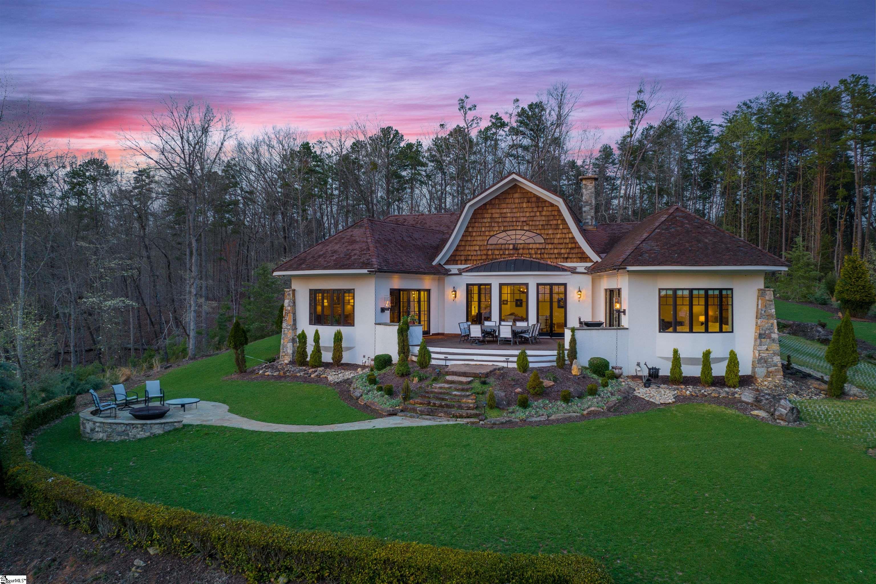 A 300 foot-long driveway leads you past a professionally designed and landscaped lawn to this astonishing house at 175 South Falls Road in the Reserve at Lake Keowee. You will feel like you are on the streets of Europe – all while in the wilds of South Carolina – as you pass a variety of 0rnamental trees, shrubs and plants, beautiful gardenias and tea tree olives, extremely aromatic, dwarf boxwoods, butterflies shrubs, lilies, peonies shrubs, Deodar cedars, Golden spruces and an array of Bonsai trees in the front of the house. The house is situated on two acres filled with red oaks, white oaks, hickories, tulip poplars, black cherries, dogwood trees, mountain laurels, persimmon trees, wild black raspberries, wild blueberries, wild muscadine grape vines. Just when you think you’ve seen everything, you will find a courtyard covered with herringbone brick pavers and circular Doggett mountain stone feature that can be used for a bird’s bath or water fountain at the top of the driveway. Are you ready to enter the house? Walk through the Borano custom made double leaf Mahogany doors to a house drawn by James Seward, who designed houses in the Cliffs as well. It has been built with insulated concrete forms, filled with concrete, and reinforced by steel cables and rebar, which makes a home incredibly strong, almost 12-inch thick walls. Because of this, the house is extremely quiet, very well insulated, and highly energy efficient. The foyer featured a half round wall, covered with a textured finish with the coat room and a powder room to the left and right. The great room features a 20-foot tall ceiling wit, custom Douglas Fir timber beams with curved brackets, a custom Dogget mountain fireplace, herringbone firebox, constructed with Isokern fireplace system made with volcanic material from Iceland with Dogget Mountain Stone columns in between arches, supporting arches and timber beams The kitchen features a double groin vaulted ceiling, merchant lantern with glass dome chandelier, a custom made China Cabinet with walnut wood backing, and solid walnut and Carrara Marble counter tops, interior illumination, fully extended drawers. Two Bosch dishwaters, a subzero refrigerators, a wolf single burner gas cooktop and a Gaggenau Induction cooktop highlight the appliances. It also has a pantry and root cellar. Three bedrooms include a luxurious main suite that includes cove ceilings, texture finished walls, Mahogany custom pocket door, a panoramic bay window, his and hers closet and a bathroom featuring a Sanijet pipeless spa bathtub. Still want more? It also has a three car garage and work area with utility sink as well as a patio great for watching sunsets and views of the lake. A once in a lifetime find!