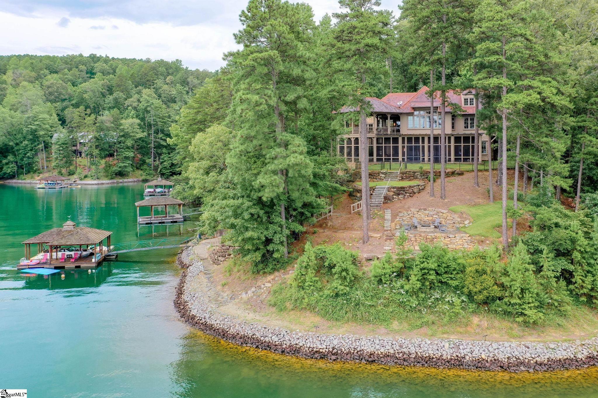 Step into a world of architectural brilliance at the Reserve at Lake Keowee. 136 S. Falls Rd. is a "ONE OF A KIND" FULLY FURNISHED, 5BR/5.5BA waterfront home that melds rustic charm with modern architecture! Welcome to your dream lakefront oasis, located on one of the "Hands Down, BEST" lots on Lake Keowee. This stunning, "private" property offers the perfect blend of luxury and natural beauty, with breathtaking views of the sparkling blue water, mountains & lush greenery. To truly experience the uniqueness of this home, you must see it for yourself. Vaulted ceilings with post and beam accents, large combination living room/dining room/kitchen area with access to the covered porches, floor-to-ceiling glass windows and custom pocket doors seamlessly blend indoor and outdoor spaces giving you amazing 180-degree lake views. Three floors of living space, including an Elevator, multiple indoor and outdoor recreation areas, wrap around enclosed screened in and covered porches with fireplaces. The covered porches and terraces account for more than 3000 sf. The third level includes an additional Bonus/Mancave/Playroom area with 5th bedroom and full bath. Rare materials were used to create this masterpiece, that was voted the 2008 Designer Show House by Atlanta Homes Magazine, including North Carolina stone, reclaimed barn wood floors, and extensive oak timbering. The gourmet kitchen is a chef's dream, boasting top-of-the-line stainless steel WOLF and Sub-Zero appliances, Meile Cappuccino machine, stone countertops, secondary wet bar and ample cabinetry for all your culinary needs. The Owner's suite is a true retreat, with expansive windows offering stunning views of the lake and a luxurious on-suite bathroom featuring a soaking tub and walk-in shower. Additional bedrooms offer ample space for guests, while a spacious covered balcony, with couch swings and fireplace, provide the perfect spot for entertaining and enjoying the stunning views. Of course, the Savant smart home system gives you total control of the entire home at all times. Outside, you'll find your own private paradise, with a large dock providing easy access to the 18,000-acre lake for swimming, boating, and fishing. The lower flagstone patio with a custom firepit is the ideal morning spot to watch the sunrise or roast marshmallows in the evening! This truly is the ultimate lakefront retreat, offering the perfect escape from the hustle and bustle of everyday life. Add the amenities and membership of the Reserve including the Jack Nicklaus Signature Golf Course, par 3 practice facility with driving range, Clubhouse with fine dining, pub area, wine bar, Fitness Center, Hiking Trails, Har-Tru Clay Tennis Courts, Lakeside Resort-Style Pool and Cabana, Pickleball Courts, Marina offering both slips and boat rentals, and the Market great for lunch or shopping for essentials. This gated community offers many activities including fitness classes, various social clubs, and a high-speed fiber-optic internet system in place. The Reserve at Lake Keowee is a full amenity lakefront golf community. Don't miss out on the opportunity to make this breathtaking property your own. Contact us today to schedule a private tour and experience the beauty and luxury of lakefront living at 136 S Falls Rd at the Reserve at Lake Keowee.