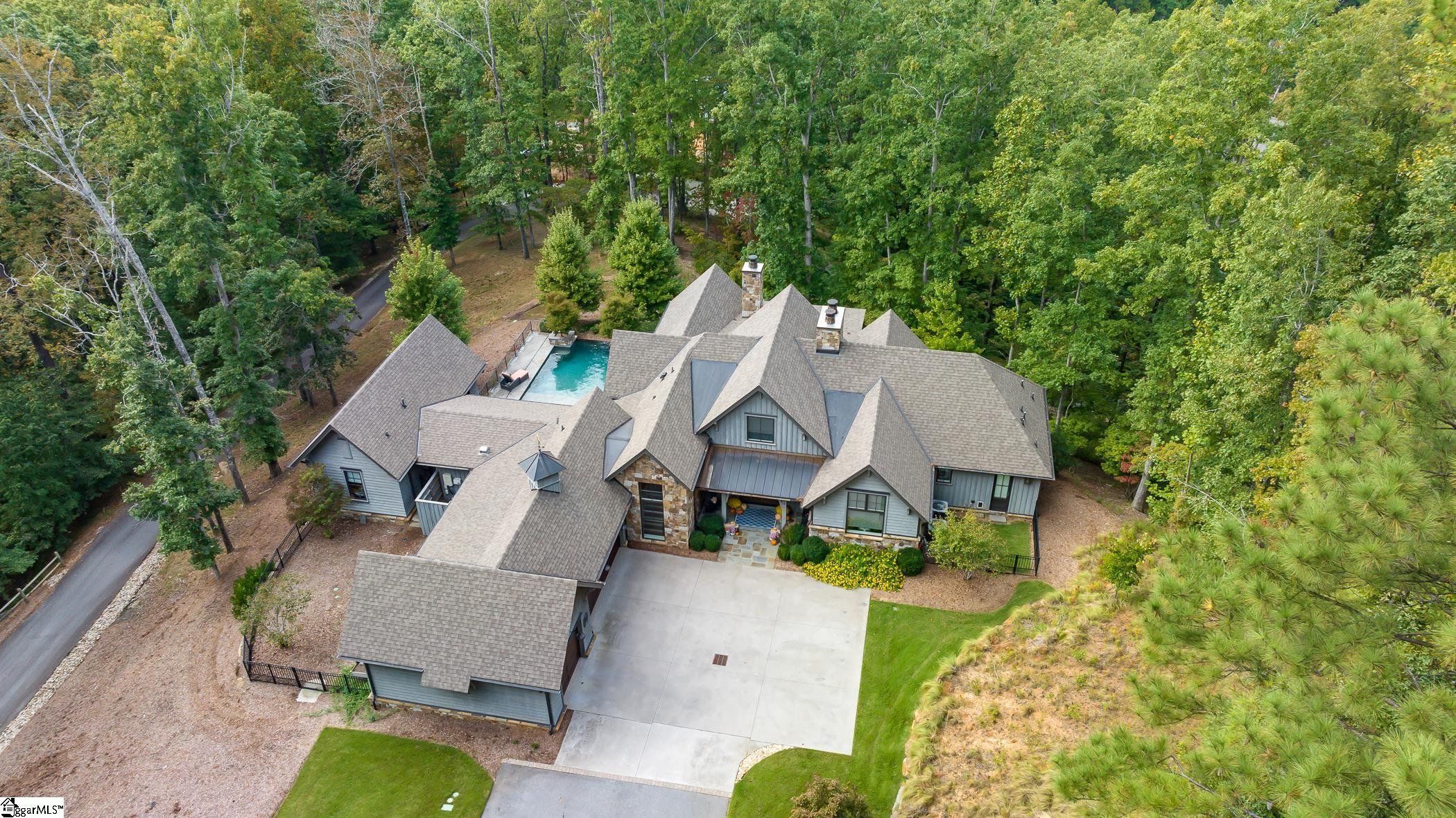 Nestled within The Cliffs at Keowee Springs, “The Sanctuary at Six Mile” was built in 2018 by Resort Custom Homes and designed by the Markalunas Architecture Group. This distinctive residence with an old-world charm sits across 3.06 acres and is surrounded by a serene, wooded setting. Offering privacy, tranquility, and seasonal views of Lake Keowee and the Blue Ridge Mountains, this retreat includes 4 bedrooms and 4.5 baths. A meandering drive along the property allows you to approach the secluded residence, complete with a 3 car garage with epoxy floors and pre-wired for an electric car. The main level is an open floor plan featuring walnut wood floors and thoughtful designer touches throughout, such as electric hardwired blinds and an integrated sound system with added modern convenience. The home is also prewired for a future generator. The Great Room, adorned with cathedral ceilings and exposed wood beams, houses a stone fireplace with gas logs and a well-positioned bar area with wine refrigerator for ease of entertaining guests. Sliding pocket wood doors open to a large screened in porch and provide all kinds of options for hosting a variety of events. The outdoor porch has retractable screens, a double-sided stone fireplace, a cozy living space that includes a porch swing, and an extra area for al fresco dining for all seasons. The kitchen, meticulously designed for culinary endeavors, features coffered ceilings, a walk-in pantry, dining space which also opens to the screened in porch and has views of the pool area. Highlighted by a large island with seating for six, also includes a built-in microwave and warming drawer. There are high-end appliances throughout, a built-in Miele coffee maker, a Wolf gas-top range, a wall oven that has steam and convection capabilities and sits with a Bluestar double French door oven. Offering plenty of cooking options and family entertaining space. The laundry room is close by and allows for easy access after pool time and main floor activities. The guest house features a one-bedroom, one-bath suite. The guest house bath suite is equipped with heated floors, a garden tub, and a separate walk-in shower creating an ideal haven for visiting family or friends. The covered patio by the pool area provides a delightful space for outdoor gatherings and grilling, offering a picturesque view of the infinity pool, hot tub and soothing sounds of a waterfall. There is a fenced area off the covered patio that could be used for raised planters and gardening space. The owner's suite is on the opposite side of the house and on the main floor. It includes a sitting area, stone fireplace and a generous bath area with garden tub, doorless walk-in shower, and heated floors. The owner’s closet features an island dresser, a dressing table area, a stackable laundry space with washer and dryer, and exterior access with a doggie door leading to a secondary fenced area. The study showcases a custom-built desk and bookcases. The lower level, reachable by an elevator or stairs, hosts 2 bedrooms and 2 baths, along with a central living room area that includes 4 built-in bunk beds for children and an outdoor covered patio. There is an extra room that can be designated for exercise equipment, a workshop or additional storage area. This property offers convenient access to the new Springs clubhouse, the Bistro, the Beach Club, Lake Club, plus a variety of amenities, including golf, pickleball, boating, hiking trails and much more. A Cliffs Membership option is available which will allow you and your family to enjoy all activities across 7 different Cliff communities.