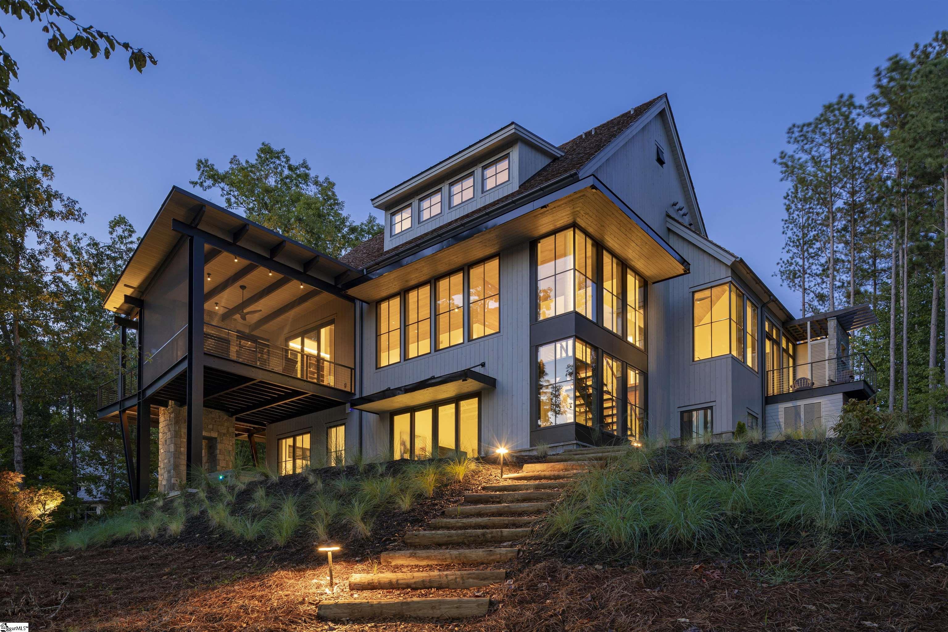 336 South Cove Road--The cover story home for "atHome" magazine's Fall 2020 builder edition is a stunning home that was thoughtfully designed by Johnston Design Group and proudly built by highly respected Ridgeline Construction Group in 2019. Located in The Reserve at Lake Keowee and nestled perfectly in a large enough cove for great views but small enough to paddleboard, kayak, or simply float and relax in peaceful bliss. This 5 bedroom, 5 1/2 bath house is the epitome of lake indoor/outdoor living and your outdoor living includes views of one of the most beautiful mountain lakes in the country, a private covered dock with boat lift and jet ski port, a Jack Nicklaus designed golf course, tennis, pickle ball, pool and country club! The main level merges indoor and outdoor spaces with views from the huge glass pivot front door right through to beautiful Lake Keowee. This level includes an open floor plan joining the kitchen, family room, bar, and even the screen porch via bi-folding doors that make separation of this space seamlessly disappear. On this level is the owner's suite with it's own outdoor shower and separate porch, walk-in closet, and free standing tub with corner lake views enabling "single story" living for the owner. The lake level includes an additional family room, wet bar with beverage fridge and ice maker, as well as an additional three bedrooms and three full baths. Two of the three bedrooms downstairs are en suites, and the third features built-in bunk beds with an adjacent bathroom. With ultimate convenience in mind, a second laundry room and mechanical/storage room with large freezer sits just off the family room. Sliding glass doors from the lake level family room provide access to an ironwood patio with an outdoor lounge that has panoramic lake views. To the right is an above ground spa that sits perfectly under the cover of the upper lever porch and is a fantastic nightly (or morning) relaxer. To the left, a gentle path leads you down to your private deep water dock. The fifth bedroom is a private guest suite above the three car garage and includes an en suite bath as well as a walk-in closet. A couple of favorite features of the home include a huge concrete gas fireplace with a retractable 85" TV (so it doesn't block the views when not in use) and the stunning corner wall of windows as you descend from the main level to the lower level, overlooking the lake. There's also an outdoor dining area on the porch providing the perfect venue for home cooked or chef catered dinners. Additionally, this home is situated at the end of a gently sloping cul-de-sac and has the rare combination of a flat driveway/gentle slope with a deep water dock site. Make your Lake Keowee dream come true...your friends and family will love you for it!