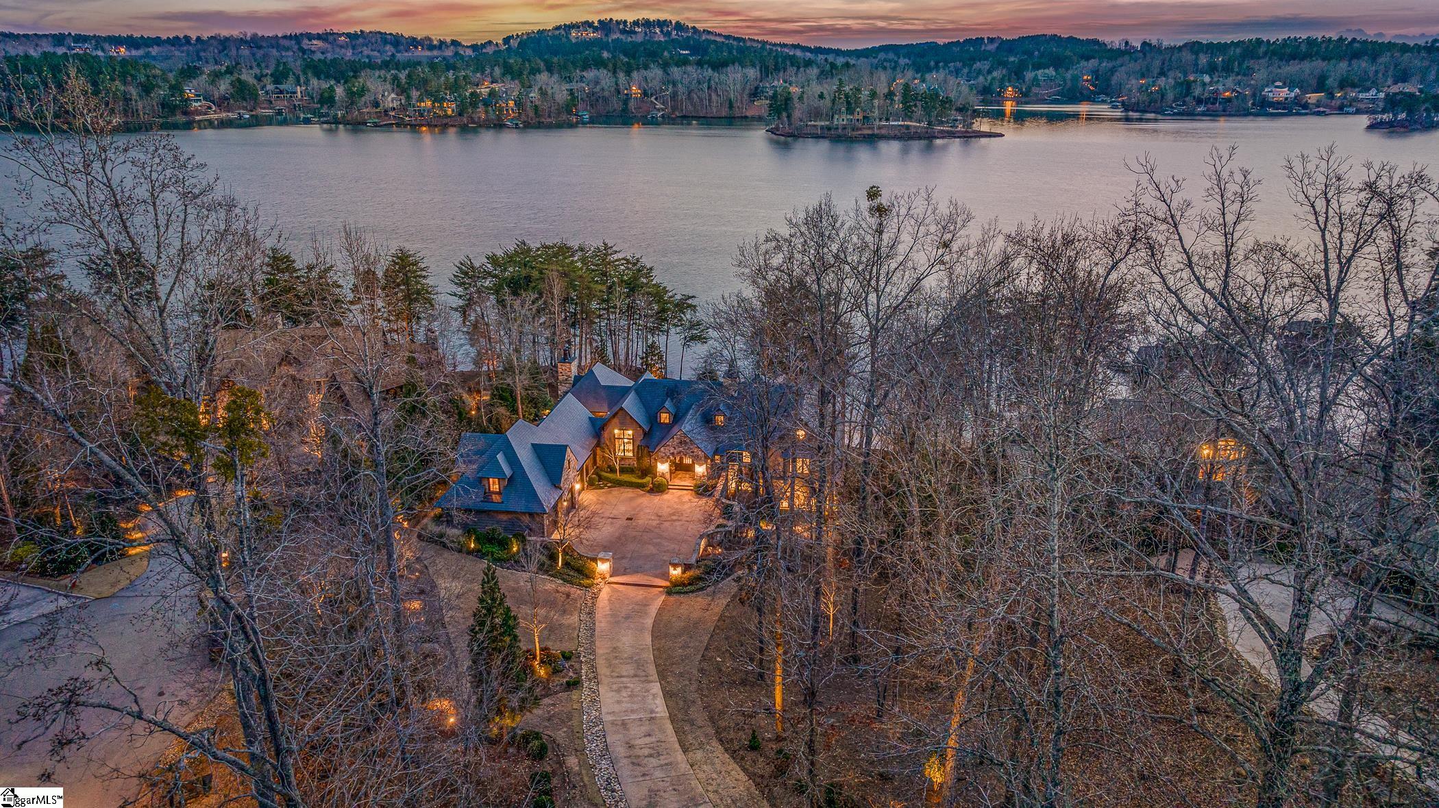 This impressive estate is a handsome mélange of old-world European charm, married to modern substance. The 6,700-foot Brad Wright designed home is strategically positioned to capture big lake views, while retaining precious privacy. Almost 180 feet of prime Lake Keowee shoreline is prefaced by a gently sloping topography, and accented by a sandy beach and custom-engineered, covered dock. Lush, lake-irrigated landscaping and impressive hardscaping includes terraces, impeccable plantings, culinary garden, and contoured aggregate driveway with turning court. Finishes throughout the 3-4-bedroom, 4.5-bathroom home are richly textured, speaking both to architectural solidity and timeless styling.  Bespoke elements include: nickel-gap paneling; Venetian plaster walls; coffered and beamed ceilings; full stone arches, accents, and fireplaces; lift-operated chandelier; hand forged ironwork, including beam strapping; French oak, wide plank engineered floors; hand forged artisanal light fixtures from Dallas; Douglas fir and antique beams; knotty alder interior doors; mahogany and cedar exterior doors.  Beyond a natural, solid stone arch, the fully free-flowing main level incorporates a broad staircase to lake level, vast great room with 20’ vaulted ceilings and elevated lake views, open den with coffered ceiling, and, beyond further, echoing arches, the dining room and palatial kitchen.  Lavishly vaulted and beamed, the kitchen generously accommodates two islands. Custom-made, hand-finished cabinets are enhanced by Ashley Norton hardware and a Travertine subway-tile back splash, which extends to the vaulted ceiling. A British range hood with antique beam, and Shaw’s 1897 apron sinks whisper “English Country House” in both kitchen and laundry room. High-end appliances include a Sub-Zero wine chiller and separate 36” fridge and freezers, plumbed Miele coffee station, dual-fuel Thermador range (with convection and steam options), and Scotsman sonic ice machine. Dutch doors frame an entrance to the kitchen courtyard, herb garden, and oversized porch with ashlar flooring, disappearing screens, and full stone fireplace. A discrete hall delineates the primary suite, with its cozy den and barn doors opening to the bathroom, where Restoration Hardware accents and numerous built-ins have been custom tailored to the space. Textural tile and stone, and a cast iron garden tub render a spa atmosphere.  Beyond the dedicated service area and entry hall and above the generous 3-car garage is en suite apartment guest lodging with wet mini bar. At lake level (beneath 10’ ceilings), a game room, family room with antique onyx floors, stone wine cellar with hammered copper trough sink and Euro Cave wine cooler, and paneled office with built-ins are joined by two heavenly en suite bedrooms, each with garden doors to patio and lake.  Further amenities include remote controlled solar shades, a 22-kw whole-house generator, paneled elevator, 4 HVAC zones, electrostatic filters, Low-E Pella architectural windows, two 80-gallon water heaters with circulator tanks, a radon mitigation system, and Simply AV surround sound and security systems. This architectural masterpiece is matched only by the admirable topography and location of its lakeland setting.