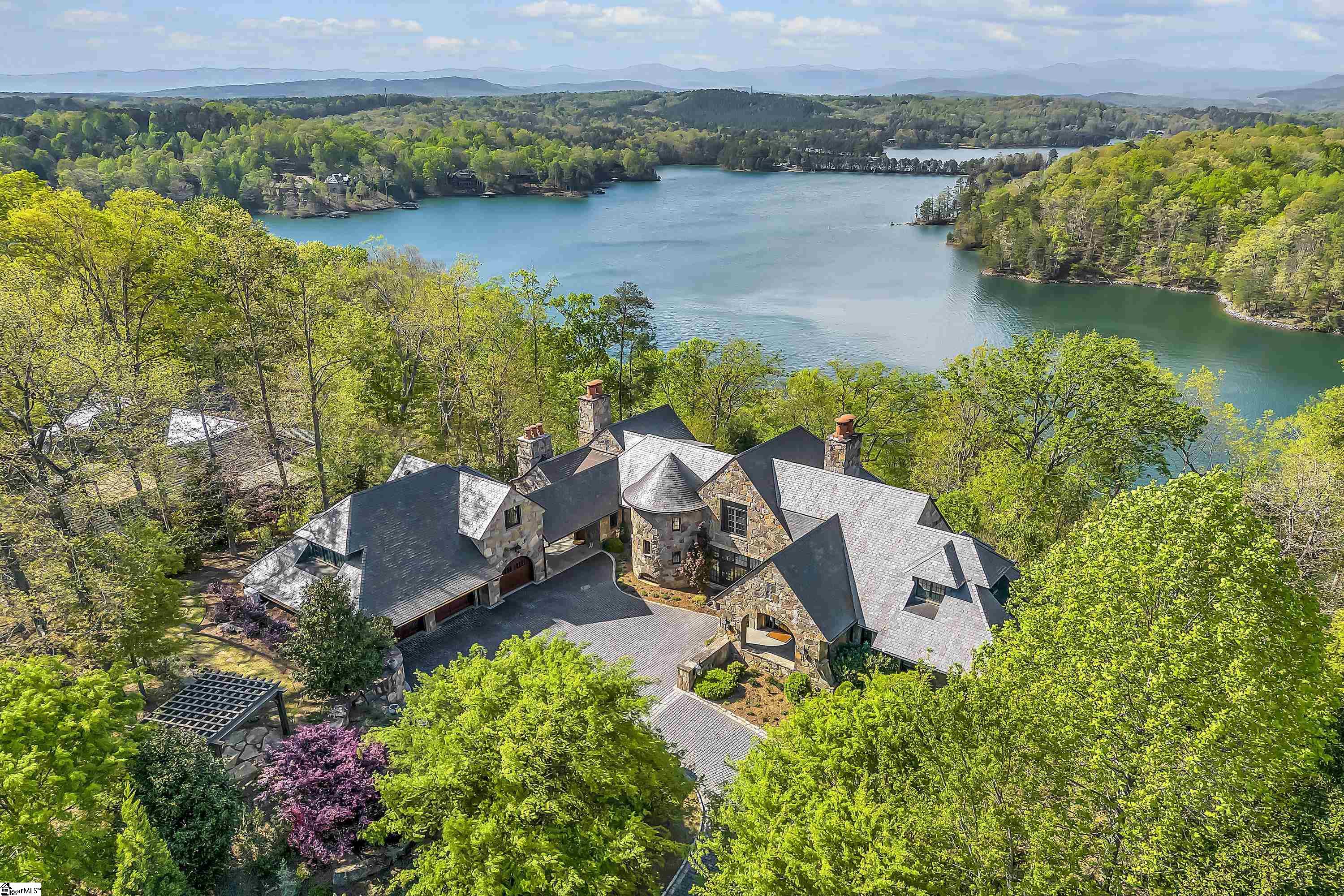 Instantly relax in the tucked away splendor of Stone Vista Manor with open, panoramic water views in The Reserve at Lake Keowee! Driving up the cobblestone courtyard, Stone Vista Manor’s massive stone arches welcome you through the foyer into the main living room that showcases some of the best views of Lake Keowee and the Blue Ridge Mountains.  Designed by Brad Wright and built by Morgan-Keefe Builders, this home is designed to provide special pockets of grandeur to its residents with features like a screened in porch with fireplace, outdoor kitchen, and dining all in one place (the best room in the home!), sleeping porch off the master bedroom, curved wine cellar under the spiral staircase, English pub style den and billiards room, and covered heated swimming pool installed in 2019 with a full bathroom to rinse off just steps away. The interior was thoughtfully curated by ID Studios Interiors in Greenville, with the landscape shaped by Barry Cosgrove Landscaping.  Live at ease in the home’s 4 bedrooms, 6 full baths, 4 half baths, and bunk room that sleeps four. The master includes his and her baths on the main floor with a laundry room just around the corner. Also on the main floor, the high ceilings in the living room feature reclaimed beams from an Ohio Mennonite Farm. The kitchen cabinetry conceals the refrigerator, separate freezer, and first-rate Miele appliances, giving the space a clean and refined look. Off to the side, a mudroom provides room for umbrellas, coats, and extra storage.   The third level holds a separate craft room and separate office, all with built-in storage for supplies, files, and more, and the home’s elevator allows seamless access to all three floors.   On the lower level, you’ll find an inlaid compass at the base of the stairs next to the wine cellar before entering the English pub and billiards room. Lofty ceilings feature reclaimed Cypress from the Everglades and more expansive views of the lake. Built for entertainment, the lower level also hosts a separate sitting room, full kitchen, and full bath where downstairs guests can make themselves right at home with access to the covered, heated swimming pool that overlooks the lake.  The detached 3 bay garage offers plenty of space for your vehicles or working space and includes a half bath. A carriage house apartment is above the garage, perfectly suited for a caregiver, housekeeper, or guests.   Stone Vista Manor makes for an ideal retreat for those who appreciate quality, custom craftsmanship and attention to detail. With stone arches inside and out, a slate roof, exterior mahogany doors, Morgan Creek Cabinets, and accents from Charles Calhoun Design & Metal Works, this home is built to last and serve your luxury lifestyle.   Positioned on 1.34 acres with tons of outdoor space, you’ll love living in the incomparable Reserve at Lake Keowee which offers over $100 million in world-class amenities: Jack Nicklaus Signature Golf Course, Orchard Clubhouse with fine dining, Fitness Center, Several Hiking Trails, Har-Tru Clay Tennis Courts at the Tennis Center plus Lawn Tennis on the Great Lawn, Pool and Cabana, Settlement Village Pool Pavilion, Pickleball Courts, Marina, and Village Market for casual dining. A Reserve membership, offering access to these world class amenities, is available for purchase with the home.  Get to the lake in under two minutes with your own full Kroeger Marine covered Dock and Tram access, enjoy the beautiful waters of Lake Keowee all year round.