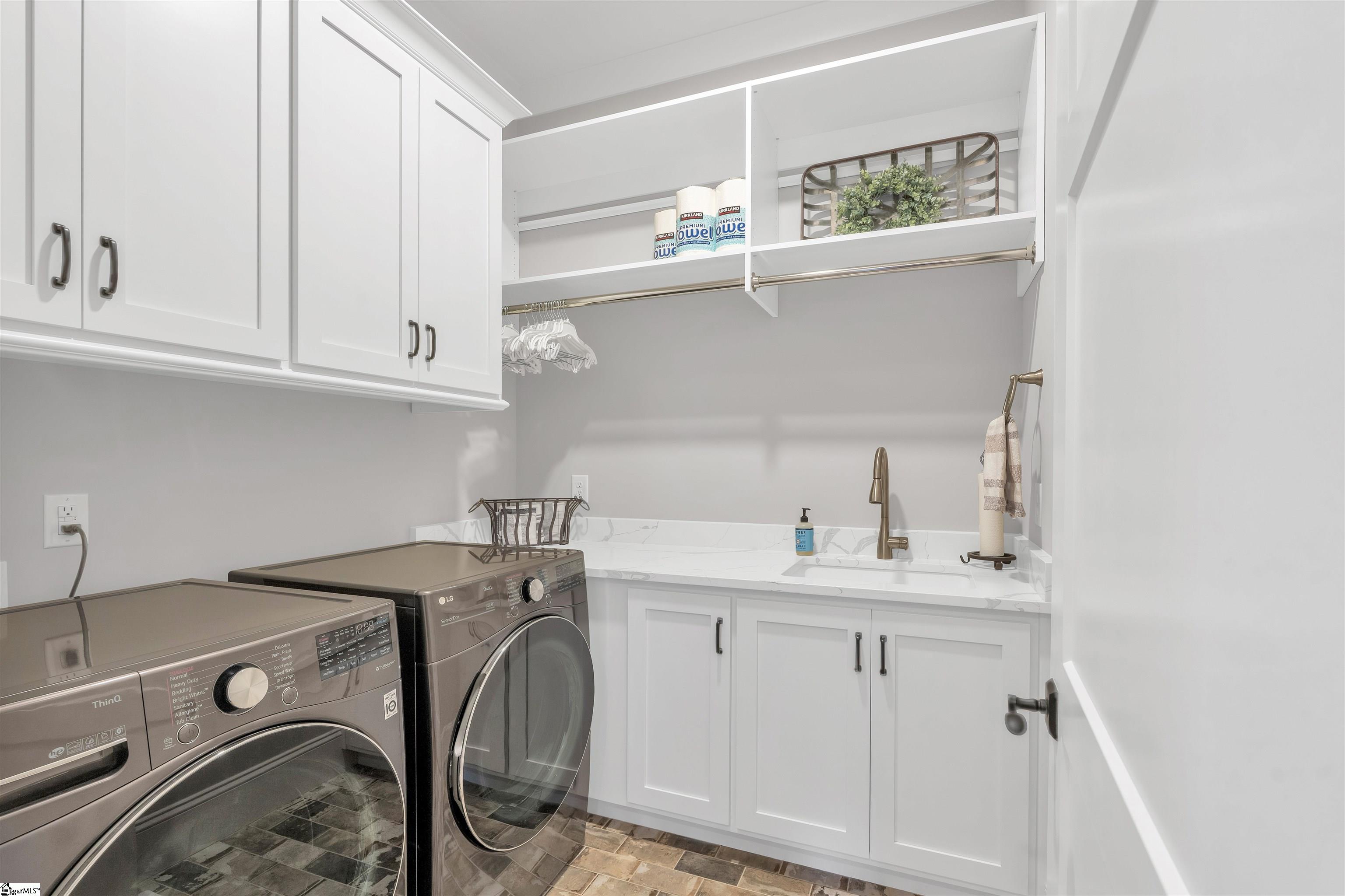 Laundry room across the hall in the primary wing with extra cabinet space, folding and hanging area, and laundry sink.