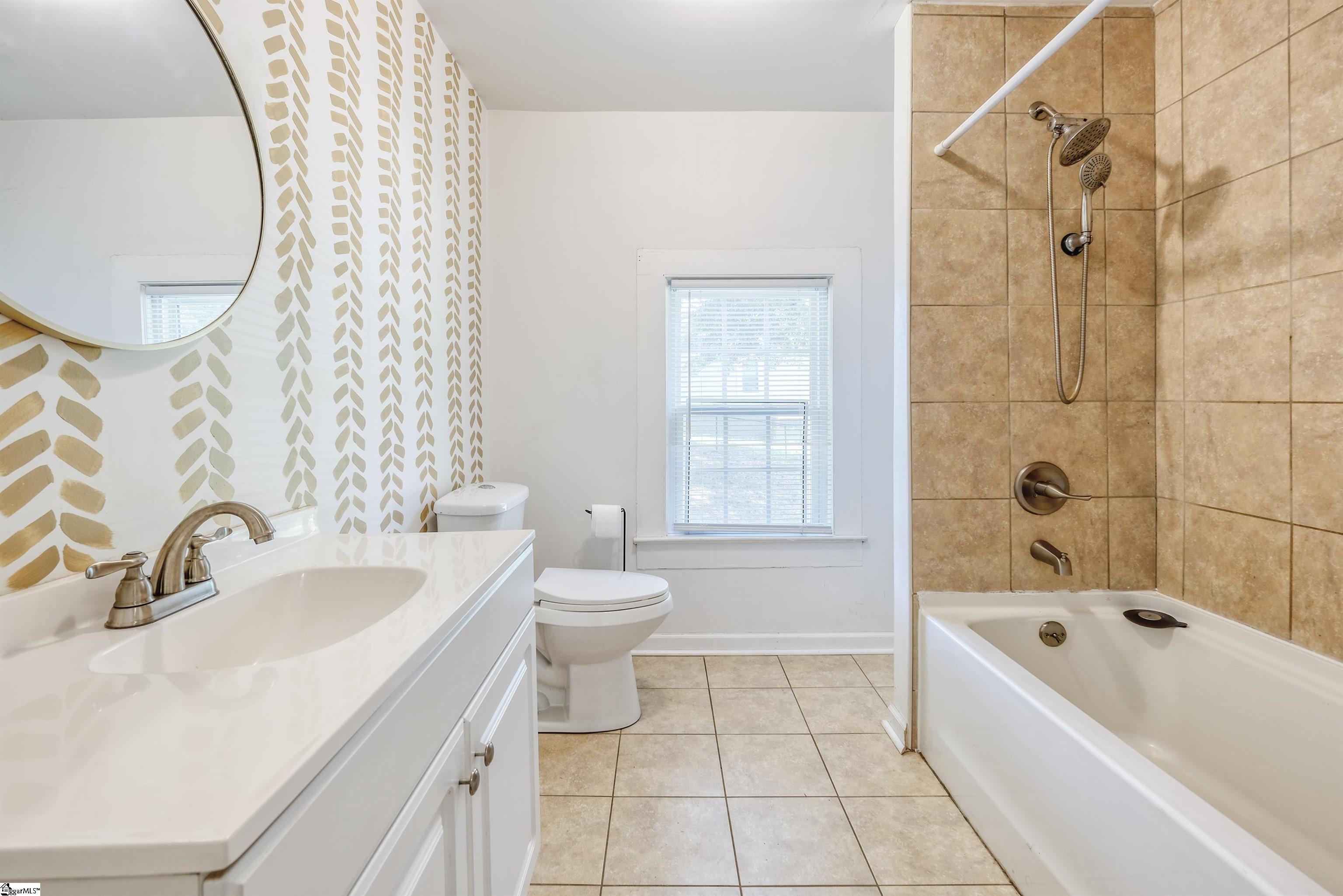 Full bath with tile shower/tub combo, tile flooring and wallpapered feature wall.