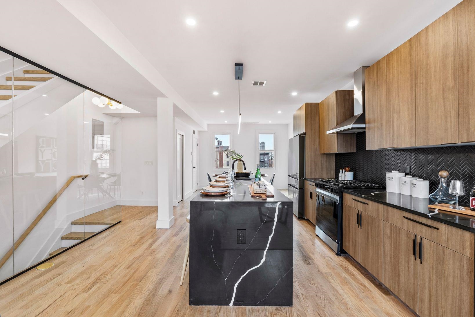 Discover the perfect blend of sophisticated design and urban convenience in this strikingly modern duplex condo, nestled on a quiet side street between Palisade and Central Avenues. Featuring dramatic architectural elements and sleek, clean lines, this home offers an expansive two-story layout designed for effortless living and entertaining.  The open-concept main level is anchored by an oversized double waterfall island, seamlessly integrating defined living and dining spaces. Glass railings and a floating staircase add to the contemporary aesthetic, with a stylish powder room on main floor. The chef's kitchen boasts bold black quartz countertops, a tiled backsplash, stainless steel appliances, and custom cabinetry, with an oversized island offering seating for four.  Upstairs, a glass-walled staircase leads to three spacious bedrooms and two luxurious full baths. The king-sized primary suite features a spa-inspired ensuite with black and white marble tile, a glass-enclosed rain shower, and an oversized floating vanity. The second bath exudes tranquility with wood-toned tiles, an extra-deep soaking tub, and dual showerheads.  Perfectly positioned for commuters, this home is just steps from Hoboken Stairs, 2nd Street Light Rail, Congress Street Elevator, and Journal Square PATH. Enjoy the vibrant neighborhood with coffee shops, restaurants, farmer's markets, Pershing Field, and Riverview-Fisk Park offering breathtaking NYC skyline views.  Deeded parking space available for purchase. **Reach out to our preferred lender e for special financing programs, offering $8, 000 to 22, 000 grants for down payment assistance or closing costs.**