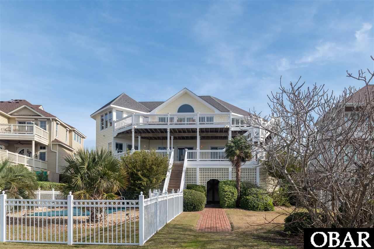 Spectacular views of the Roanoke Sound and historic downtown Manteo from this executive custom built Sound and Canal front home. A spacious home that features 6 BRS, 3 FULL BA, 2 HALF BA, and is situated on one of the best lots in Pirate's Cove. Multiple large decks (covered & uncovered)  take advantage of the amazing views and the private backyard pool oasis. The 50' private boat dock is steps away directly behind the home, and conveys to registered boat owner. This home is very spacious with over 4,100 HSF with an open concept, tall cathedral ceilings, reverse floor plan, and numerous windows to bring in the sunlight and panoramic views. Private pool, elevator, boat dock, and 2 gas fireplaces. Top floor features living room with gas fireplace, custom kitchen and dining area with several accesses to the large upper deck. Mid level features separate living room with 2nd gas fireplace with access to the large covered deck, and has a hot tub and swing for relaxing and watching the incredible sunsets over the sound looking at historic downtown Manteo. Lower level has laundry area, desk & half bath with dry entry. Under carport parking with outside shower and plenty of space for parking while guest are visiting.  Pirate's Cove is a gated community which has two private pools, tennis courts, playground, Tiki Bar, Blue Water Grill & Raw Bar, World Class Marina & Pavilion, fitness center, and clubhouse. Fabulous home in an excellent location. Close to shopping, restaurants, Jeanette's Pier, beach access, and downtown Manteo.