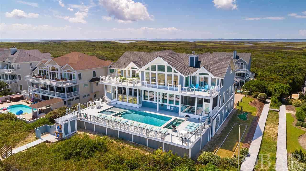 This truly spectacular Pine Island oceanfront will simply take your breath away!! With sweeping ocean and sound views, this home has everything you would ever want or need in a luxury beach retreat! Located on a quiet cul-de-sac, you will enjoy the private and very quiet beaches, right outside your back door. Built by Olin Finch with amazing attention to detail in every feature, this property will be sure to please even the most discerning buyer. Boasting ten spacious master bedroom suites with an ideal layout from top to bottom. These owners have meticulously cared for this very special and unique property so there is not a thing you have to do but enjoy it! You can even take in the fantastic ocean views from the custom mid-level pool, complete with an outdoor fireplace built in! The outdoor oasis is the perfect place for everyone to soak up the sun and relax on the beach! Poolside covered outdoor kitchen with three large grills, fridge, icemaker and outdoor TV, outdoor speakers, and a ten-person hot tub. The elevated pool even has a swim up bar, baby pool, and lighting features for nighttime swims! There is even a putting green and bocce court are available to enjoy in the yard. This incredible home offers so many perfect outdoor lounge areas, you can watch the sunrise over the ocean and enjoy those gorgeous Outer Banks sunsets overlooking the sound. Two screened in porches (one on the sound and one on the ocean). The top level is where you can gather large groups together for meals and entertaining with a huge custom gourmet kitchen with top-quality stainless-steel appliances (Viking gas range), ice maker, three ovens, two dishwashers, two smart refrigerators, warming drawers, appetizer sink, teak coffee bar, granite countertops, and plenty of seating at the two large dining tables and bar top seating at kitchen counter. Gas fireplace in the living area for those cozy, cool evenings and a wet bar with wine cooler so you don’t have far for a beverage while you watch a movie or game on the large living room TV. Every room in this house is simply amazing and beautifully decorated.  The spectacular top floor master bedroom is truly unique, with ocean to sound views and a gas fireplace. When the sliding doors between the bedroom and bathroom are open, there are ocean views from the large, tiled shower with multiple showerheads. Have a restorative soak in the whirlpool tub after relaxing in the private sauna. Powder room located off living area. The middle level has a rec room with pool table also includes comfortable seating, a TV, and a wet bar with a full-size refrigerator. The screened porch is located just off the rec room. A half bathroom is nearby for convenience. All the five bedrooms on the middle level is a master, each with a private bathroom. Each bathroom features a beautiful upscale tiled shower, some with multiple sprayers. The lower level also includes bedrooms and entertainment areas. Each of the four bedrooms on this level is a master, with a private bathroom with a tiled shower. One of the luxurious master bathrooms features multiple showerheads and sprayers, a rain shower, and whirlpool bathtub. Take family movie night to the next level in the large theatre room. Sink into one of the 16 leather recliners in the state-of-the-art theater. A wet bar with a full-size refrigerator is located just outside of the theatre room for convenience. The laundry room and a half bathroom complete the lower level’s interior. Step outside of the lower level to play ping pong or checkers on the lower-level deck. This luxurious and stunningly beautiful home has everything and more!!!