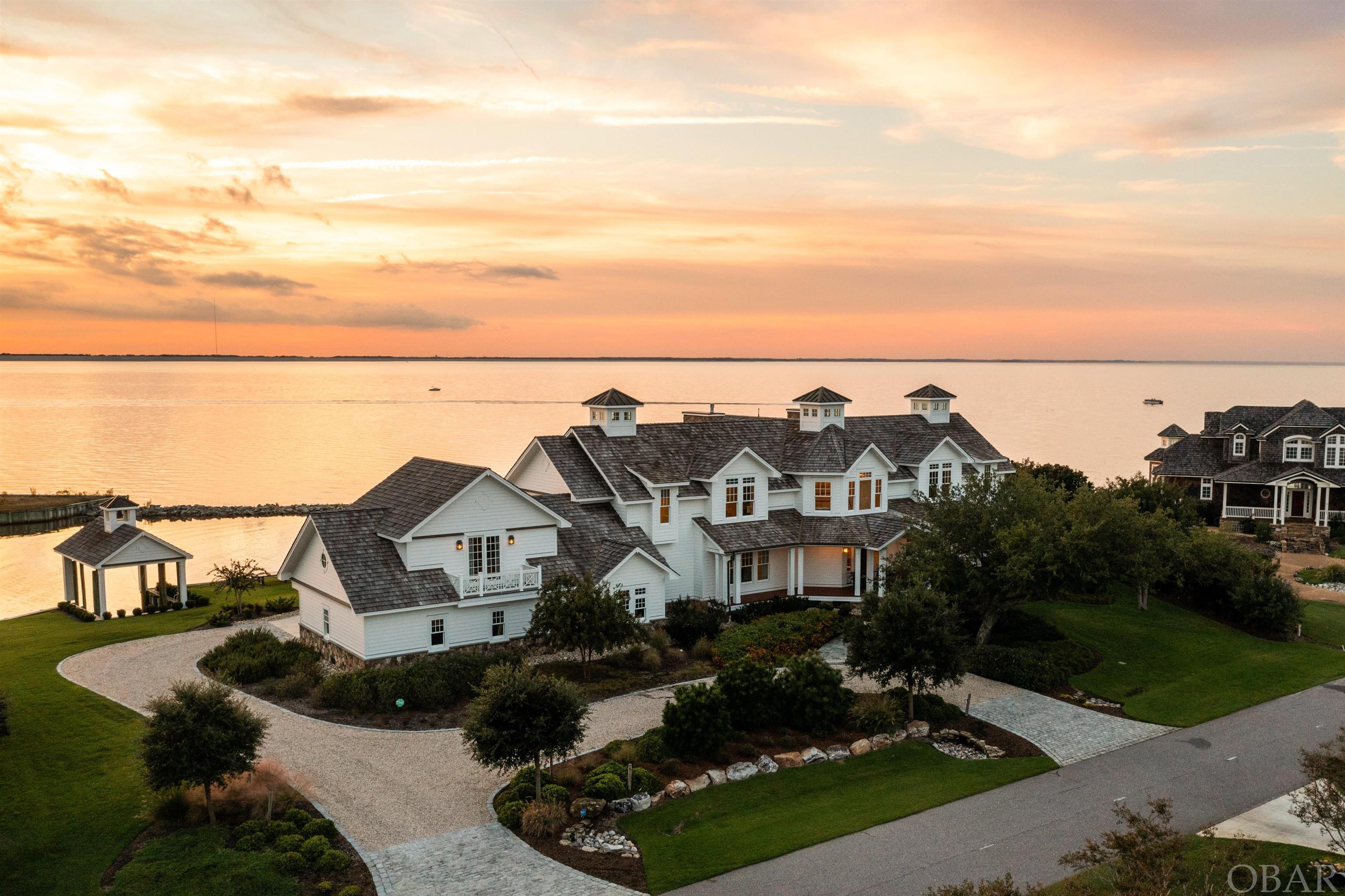 Mill Point is one of the finest primary residential properties on the Outer Banks. The home sits high on a ridge overlooking its own harbor and offering uninterrupted panoramic views of the Currituck Sound. This is the only home on Gallop Harbor, and it boasts a boathouse with belfry and bronze bell, 430 feet of direct waterfront, a 30’ flagpole, mature shrubbery and inground heated swimming pool and spa, with waterfall and accent features.  Situated on the northern tip of the Martin’s Point peninsula, this westward facing lot offers stunning water views from every room.  Croft Hall Design and the owners meticulously designed every aspect of the property, and Sandmark Custom Homes transformed their dream plans into reality.  From its classic architectural design with cupolas, decorative dentil molding, and copper accent flashing, to state-of-the-art modern conveniences, including an elevator, to provide step free access from the attached three car garage to both levels of the home.  Whimsical touches like secret doors in bookcases, and a spiral staircase to provide a short cut to the master bedroom, plus more traditional features including coffered ceilings, custom cabinetry and an inlaid compass rose design in the walnut flooring, complete the look of high quality and exceptional craftsmanship. Energy efficient geothermal heating and cooling, LED lighting and impact glass windows and doors throughout are just some of the features that will attract the discerning buyer. Despite very light use since its completion, the residence and grounds have been meticulously maintained.  For a complete list of features, specifications, and detailed floor plans, please contact your OBX Realtor. Pre-approval or proof of funds are required prior to viewing. Unique and special properties like this are rarely offered for sale on the Outer Banks. Here is a great opportunity to enjoy the best of the best in Outer Banks residential living!