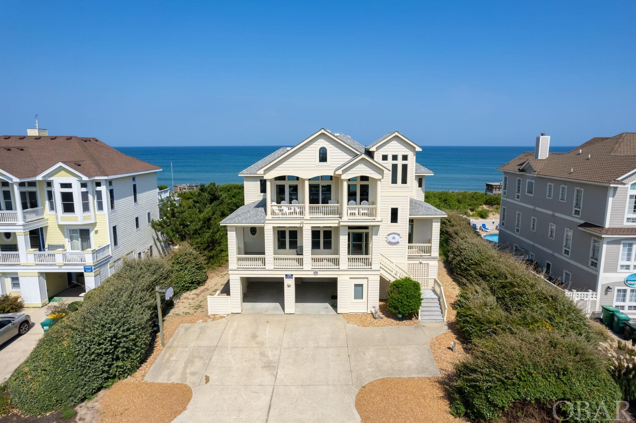 Breathtaking ocean and sound views can be yours with this 6 bedroom, 5.5 bath home located in prestigious Pine Island.  This exquisite home features a large open floor plan, cathedral ceilings, ships watch, wainscotting throughout the hallways and stairwells, multiple decks on both the east and west elevations, game room with kitchenette, pool, hot tub, and private walkway to the beach with a dune top deck.  Fronted by the Currituck Sound and Audubon Nature Preserve, and flanked by the Atlantic Ocean, this 4500+ square foot vacation home is all about the views.   The cathedral ceilings and oversized windows on the upper level bring light and panoramic views into every corner.  The unbroken sightlines run from the Great Room with oceanside sun deck, into the designated dining area with covered sound side balcony, into the kitchen with its abundance of counter space and additional seating in the breakfast nook and island.  Adjacent to the kitchen is a convenient pantry and a powder room. The midlevel features 3 en Suite bedrooms, all with private bathrooms complete with double sinks and jet tubs.  Two of these large bedrooms offer ocean views and covered deck access, and one even has access to the sound side covered deck.  The third en Suite offers views out over the Nature Preserve and Sound.   Additional guest rooms are on the ground level connected by the game room with a kitchenette.  A pyramid bunk room with covered porch access is next to a full hall bath on one side of the game room, and a double pyramid bunk room shares a full bath with another large bedroom with covered porch access on the other. But there’s more!  Outside is the expansive pool and hot tub area befitting a home of this size.  (The outside shower and convenient outside half bath are adjacent.)  The 16x30 saltwater Gunite pool is the perfect spot to cool off after a day spent on the uncrowded beach.  The dune top deck at the end of the private walkway offers a relaxing resting place to enjoy the magnificent ocean views with a picnic lunch or evening cocktail.   An array of amenities are offered in this upscale Pine Island community, including 2 outdoor pools, beach club, tennis, volleyball, and more.  Located between Corolla and Duck, the central location affords an easy route to the unique attractions, dining, and shopping of both communities.