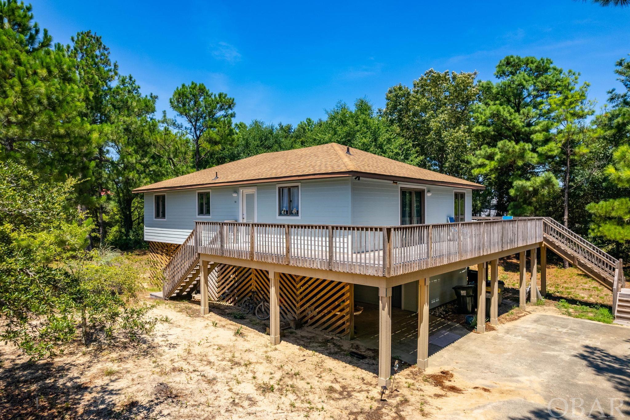 Check out this amazing Chicahauk opportunity! Located just a short distance to the Chicahauk Trail beach access which includes private parking. Nestled in the trees on a large private lot, this home has a lot to offer. The carport and covered entryway leads to the newly enclosed and permitted ground floor living space. This area provides the 4th bedroom ensuite, a den, and laundry facilities. Heading up the new interior staircase, you will find an open living, dining, and kitchen concept with vaulted, wood-beamed ceilings, 3 bedrooms, and 2 full bathrooms. There is new carpet throughout the home and gorgeous hardwood in the kitchen. The oversized primary bedroom has a cedar lined walk-in closet, private ensuite with new flooring and vanity, and sliding door access to the wrap-around porch. The other two bedrooms share a jack and jill bathroom on the opposite side of the living room. The spacious screen porch is desirable for long summer nights enjoying the outdoors. The entire home was recently re-sided with cement fiber board and painted. Come see for yourself today and start enjoying all Southern Shores has to offer!