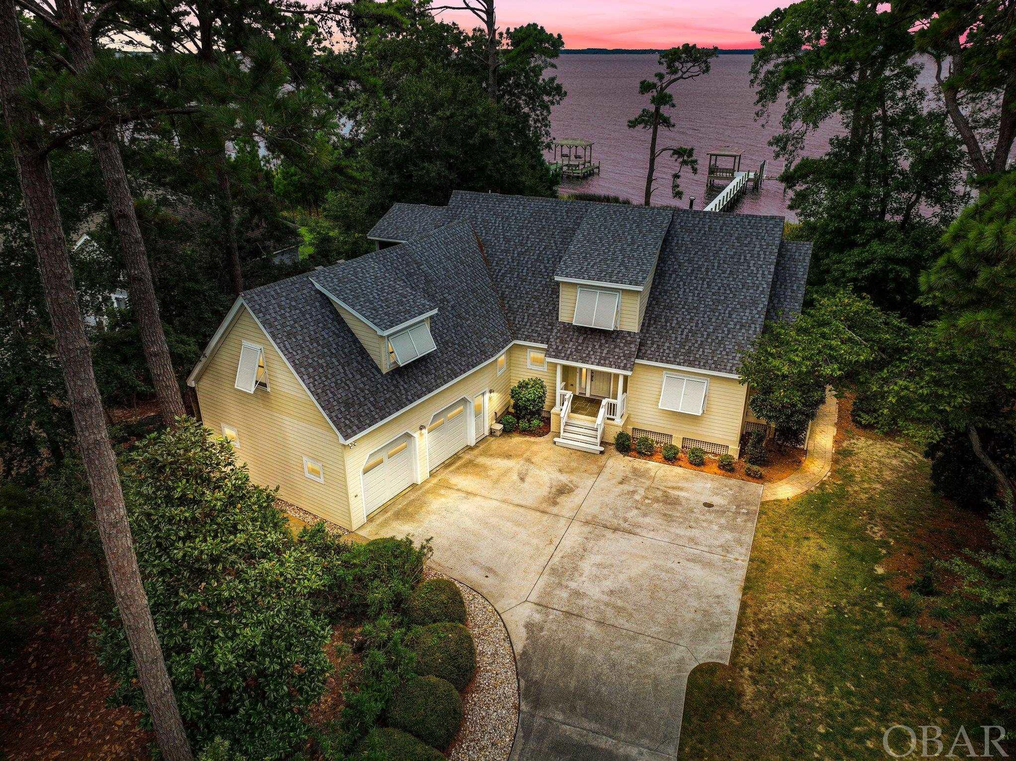 Coastal living at its finest. A 4 bedroom, 3 full bath, 2 half bath coastal home tastefully renovated and cared for in the secure enclave of Martin's Point. On the first floor you find expansive windows overlooking the Currituck sound inviting the outdoors in to your comfortable living room with vaulted ceilings & a gas fireplace, custom kitchen, dining area, sunroom, laundry room, primary bedroom suite and two car garage. Upstairs we follow the catwalk to a finished room over the garage with private bath, a guest bedroom with private access to the screened porch, and a third bedroom currently setup as an office with a private half bath. Outdoor space includes a sun deck with retractable awning that seamlessly flows to the outdoor fire pit, grill area, and private dock with gazebo. Take in the awe-inspiring, unobstructed water views and sunsets daily. Access to the sound, a secure community and home designed for entertaining, make this private oasis a distinctive opportunity to live the unique Outer Banks lifestyle.