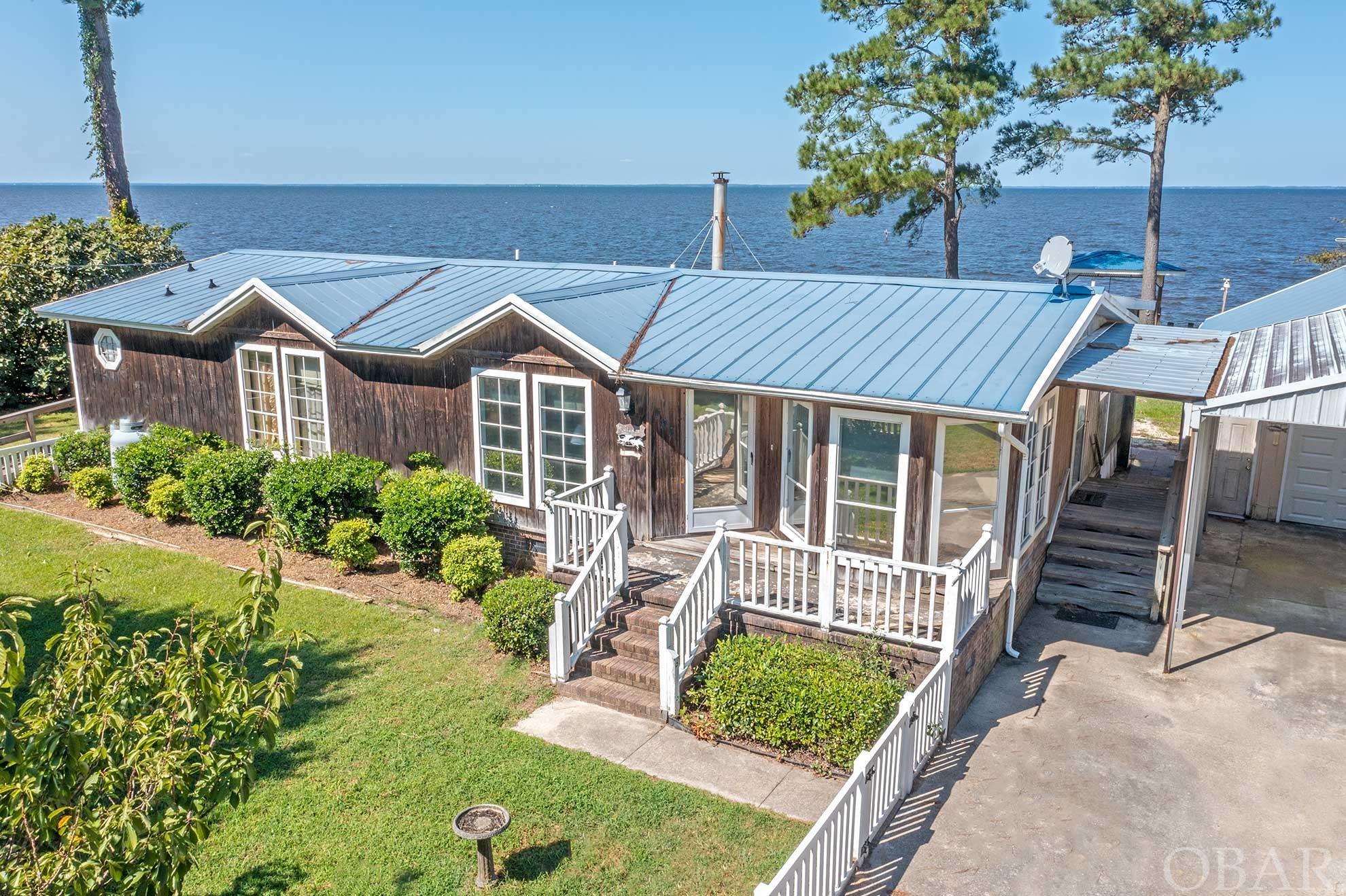 Panoramic waterfront views located on the Albemarle Sound in X-Flood Zone! Beautiful location for year round living or weekend getaways. This three bedroom, two bath home is nestled on a half-acre lot, perfect for just relaxing or a mini waterfront homestead far away from the hustle and bustle. Enjoy an open concept design inside this ranch style double-wide manufactured home. The kitchen has Corian type counter tops, stainless steel appliances, a breakfast bar as well as a separate dining room with a bay window. The living room features a vaulted ceiling which opens onto the covered deck with water views, a fireplace, a propane heater and a wood burning stove. Large master bedroom has a private covered deck overlooking the sound with a wheelchair accessible ramp. Master bathroom has an accessible shower, floor to ceiling storage and a double vanity. Property features a detached garage, a huge carport and two bay pole barn, all with blue metal roofing. Also a chicken coop, garden bed, outside fish cleaning sink, a mature fig bush and grape vine that were full of fruit this summer. Separate power pole for motorhome set up; possibly set up an Airbnb for extra income potential. The bulkhead is approx. 175ft, vinyl fencing in the front yard and covered decking across the back of the home with amazing water views. A waterfront gazebo with a wooden swing for fishing, launching your kayak, or just enjoying the vistas. Affordable waterfront living about an hour from the Outer Banks, and 30 minutes to Manteo. This area is an outdoorsy paradise with fishing, boating and abundant wildlife! The historic, waterfront town of Columbia is quaint with a small marina, shopping, restaurants, and cultural arts with Pocosin Arts School of Fine Craft as well as Pocosin Lakes Wildlife Refuge.  Come make this your waterfront dream home!