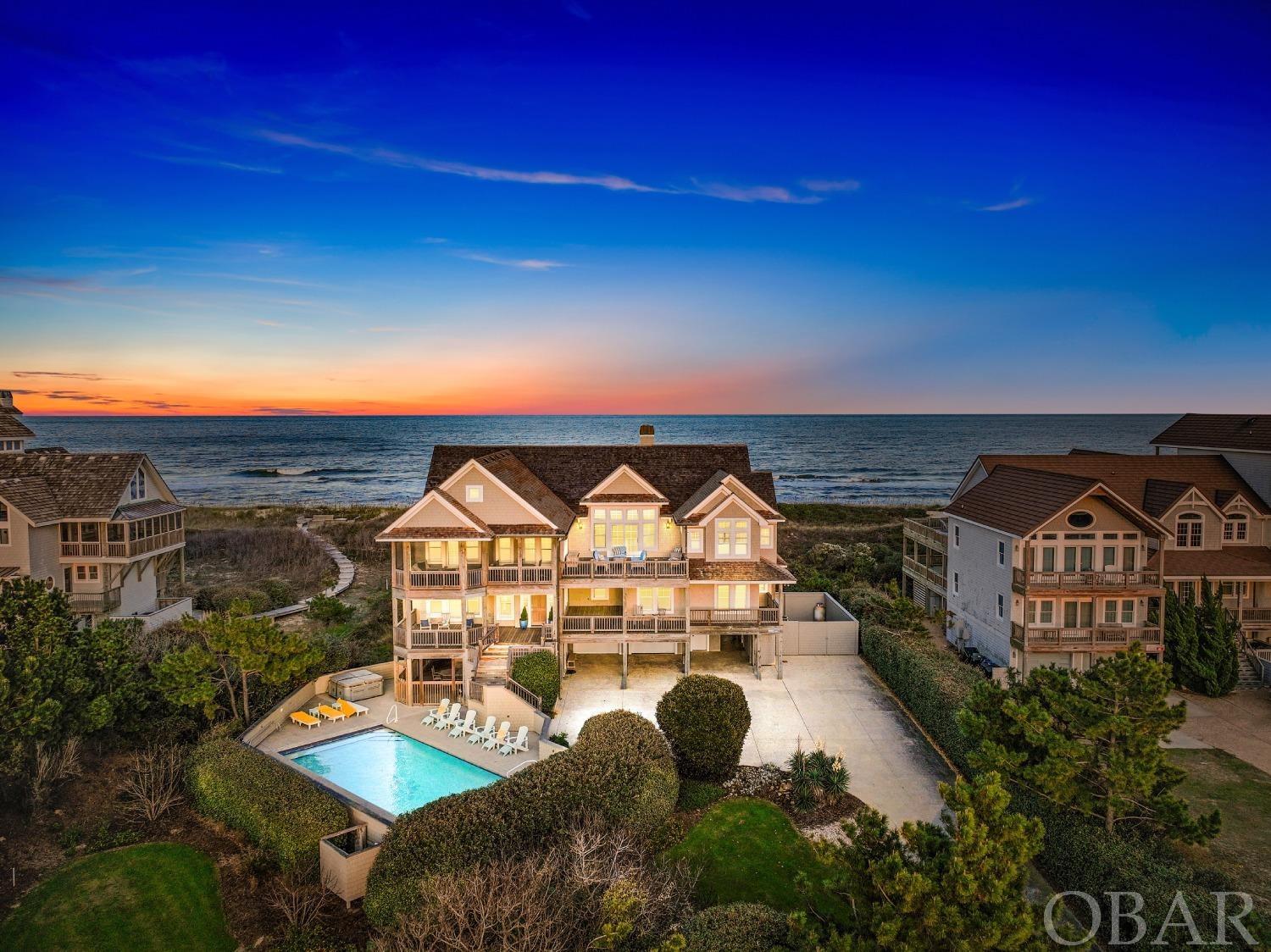 This beautiful Palmer’s Island oceanfront estate, the epitome of luxury, is just one of thirteen homes in a quiet neighborhood that spans one of the Outer Banks' most exclusive and private stretches of shoreline. Situated on a wide, elevated lot, the estate offers breathtaking panoramic views of the ocean and the sound. Each level's extensive decking provides plenty of space for enjoying the sunrise over the ocean and the spectacular Outer Banks sunsets that light up the sky over the sound. Built by one of the top builders in the area, the interior features an open floor plan, intelligently designed to take full advantage of exceptional sight lines, with abundant natural light made available through the many oversized windows. Common areas boast elaborate décor and top-quality furnishings, surrounded by exquisite shiplap walls and high ceilings, along with custom flooring. Other amenities include a central vacuum, security system, and even an enclosed area for storing/parking a boat. The grand foyer, dining room, gourmet kitchen, and main family room are impressive. Spacious and well-equipped, the kitchen offers not one, but two large islands, both with sinks, and high-end stainless appliances that feature two ovens, two dishwashers, a gourmet gas top stove, an ice machine, wine and beverage coolers, in addition to a large sub-zero refrigerator, and bar-top seating that flows seamlessly into a breakfast nook on one side and the dining and living areas on the other, making entertaining large groups a breeze. A beautiful screened porch off the dining area is the perfect spot to gaze upon the sound while taking in the amazing Outer Banks sunsets. An en-suite primary bedroom offers access to the sun deck and breathtaking views of the ocean, rounding out the top-floor living area. The en-suite bathroom features a steam shower and a distinctive whirlpool tub where you can unwind while soaking in yet another spectacular view of the sound. Most bedrooms are situated on the mid-level, accessible by elevator or stairs, each spacious and offering impressive water views and access to the home’s extensive decking. Three of the mid-floor bedrooms have en-suite bathrooms, and the other two have private half-bathrooms and share a shower and tub. Yet another room on this level currently has two twin beds but could instead provide a great office or gym. The mid-level also includes a large den with a wet bar, complete with a beverage refrigerator and ice maker, as well as a TV and a large couch for lounging and watching movies or a big game. Like the bedrooms, the den also has access to the covered deck, where you can take in the salt air, listen to the waves on the beach, and relax in a shaded hammock or swing. The last bedroom is found on the first level. Spacious, quiet, and comfortable, there is a full bathroom attached. An oversized two car garage and four exterior storage sheds offer an abundance of options for storing all of your beach gear and toys, and a sizable stamped concrete driveway offers plenty of room for parking. Also on the ground level is an expansive patio area, offering a grill and outside table adjacent to an oversized custom pool and six-person hot tub. Also adjacent to the patio is a breezeway that has two outdoor showers and that flows into a private boardwalk guiding you to the beach. Palmer's Island is a premier neighborhood in the northernmost part of Duck that offers unpopulated beaches, awe-inspiring views of the ocean and sound, private access to a sound side pier that is ideal for launching your kayak or paddleboard, and the option to pay for access to the Sanderling Community's tennis courts, clubhouse and gym. Don't miss the opportunity to join this private and quiet community, located in one of the most exclusive and desirable neighborhoods on the OBX. Please be sure to check out the virtual tour of this property by copy/paste into your browser: https://my.matterport.com/show/?m=vgJjSHSBJUk&mls=1