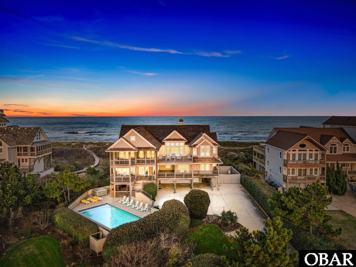This beautiful Palmer’s Island oceanfront estate, the epitome of luxury, is just one of thirteen homes in a quiet neighborhood that spans one of the Outer Banks' most exclusive and private stretches of shoreline. Situated on a wide, elevated lot, the estate offers breathtaking panoramic views of the ocean and the sound. Each level's extensive decking provides plenty of space for enjoying the sunrise over the ocean and the spectacular Outer Banks sunsets that light up the sky over the sound. Built by one of the top builders in the area, the interior features an open floor plan, intelligently designed to take full advantage of exceptional sight lines, with abundant natural light made available through the many oversized windows. Common areas boast elaborate décor and top-quality furnishings, surrounded by exquisite shiplap walls and high ceilings, along with custom flooring. Other amenities include a central vacuum, security system, and even an enclosed area for storing/parking a boat. The grand foyer, dining room, gourmet kitchen, and main family room are impressive. Spacious and well-equipped, the kitchen offers not one, but two large islands, both with sinks, and high-end stainless appliances that feature two ovens, two dishwashers, a gourmet gas top stove, an ice machine, wine and beverage coolers, in addition to a large sub-zero refrigerator, and bar-top seating that flows seamlessly into a breakfast nook on one side and the dining and living areas on the other, making entertaining large groups a breeze. A beautiful screened porch off the dining area is the perfect spot to gaze upon the sound while taking in the amazing Outer Banks sunsets. An en-suite primary bedroom offers access to the sun deck and breathtaking views of the ocean, rounding out the top-floor living area. The en-suite bathroom features a steam shower and a distinctive whirlpool tub where you can unwind while soaking in yet another spectacular view of the sound. Most bedrooms are situated on the mid-level, accessible by elevator or stairs, each spacious and offering impressive water views and access to the home’s extensive decking. Three of the mid-floor bedrooms have en-suite bathrooms, and the other two have private half-bathrooms and share a shower and tub. Yet another room on this level currently has two twin beds but could instead provide a great office or gym. The mid-level also includes a large den with a wet bar, complete with a beverage refrigerator and ice maker, as well as a TV and a large couch for lounging and watching movies or a big game. Like the bedrooms, the den also has access to the covered deck, where you can take in the salt air, listen to the waves on the beach, and relax in a shaded hammock or swing. The last bedroom is found on the first level. Spacious, quiet, and comfortable, there is a full bathroom attached. An oversized two car garage and four exterior storage sheds offer an abundance of options for storing all of your beach gear and toys, and a sizable stamped concrete driveway offers plenty of room for parking. Also on the ground level is an expansive patio area, offering a grill and outside table adjacent to an oversized custom pool and six-person hot tub. Also adjacent to the patio is a breezeway that has two outdoor showers and that flows into a private boardwalk guiding you to the beach. Palmer's Island is a premier neighborhood in the northernmost part of Duck that offers unpopulated beaches, awe-inspiring views of the ocean and sound, private access to a sound side pier that is ideal for launching your kayak or paddleboard, and the option to pay for access to the Sanderling Community's tennis courts, clubhouse and gym. Don't miss the opportunity to join this private and quiet community, located in one of the most exclusive and desirable neighborhoods on the OBX. Please be sure to check out the virtual tour of this property by copy/paste into your browser: https://my.matterport.com/show/?m=vgJjSHSBJUk&mls=1