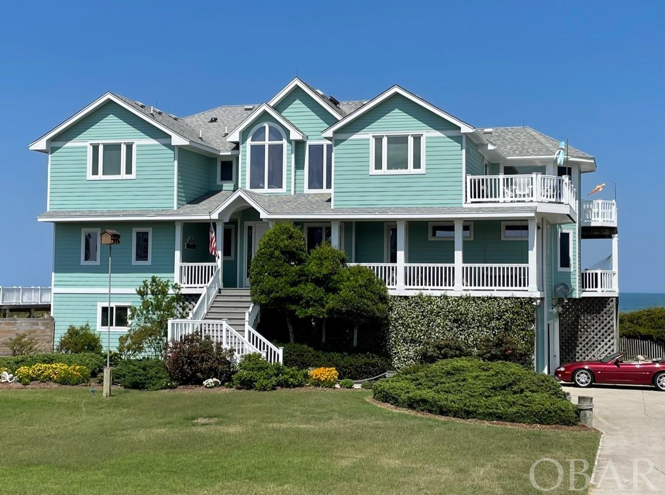 This beautiful custom oceanfront home is designed to maximize ocean, beach & lighthouse views. Located in Ocean Hill with the largest lots & setbacks in Corolla. Ocean Hill’s paved private roads protect owners from on-street parking.  Ocean Hill’s restrictive covenants protect one from 9+ bedroom mini-hotels being built in other areas.  An ideal place for  homeowners & guests. With just over 5,000 SF of air conditioned floor space, the dining & sleeping areas accommodate up to 14 guests comfortably. You enter the home from the spacious covered front porch, complete with sitting area.  The entry door opens to a large oak-floored family room. Four large windows provide your first views of the wide dune and the ocean beyond. This large family room serves as a daytime game room & a Dolby Atmos surround-sound theater after dark. Ascending the open staircase to the top level reveals the great room with spectacular panoramic ocean views of the full coast from north to south.  The great room’s granite fireplace surround and oak mantle are framed by custom oak shelving & a second surround-sound video system.  The open floor plan flows to a large dining area with views of the Ocean & Currituck Lighthouse.  This is adjacent to the spacious modern kitchen with cook island that opens to the lighthouse deck for outdoor grilling & dining with sunset & lighthouse views. The great room also opens to a large oceanside deck to watch the sunrise. The upper-level owner suite has two sitting areas: one in front of four large oceanfront windows, for enjoying the ever-changing views of sea and sky; the second faces the fireplace & TV for a relaxing private evening. This suite features separate his & her walk-in closets/dressing rooms & a large custom tiled bathroom with spacious shower area & a separate heated Jacuzzi tub.  The well-lit area features his & hers vanities & a hidden laundry chute. The mid-level has been designed to offer  separate accommodations. To the north is a large king bedroom with sitting area & ensuite bath. Next is a four-bed bunk room.  The north side also has a combined laundry/ hobby room with a full sink, desk area, built-in cabinets & cedar closet storage. The south side has an oceanfront king bed suite with walk-in closet & Jacuzzi tub; plus ocean views & deck access. Mid-level deck has a large hot tub & a shaded hammock with ocean & Lighthouse views. Across the hall is a queen bed suite that opens to a covered front porch with porch swing & seating with great sunset & lighthouse views.  The ground level features a large bonus room with king sofa bed, ensuite bath, mini-kitchen with fridge & wet bar. The garage area is for two cars out of the elements; plus a large storage area & an enclosed work room.  An elevator allows easy access from the enclosed garage area to both the mid & upper levels. All floors have deck access to a walkway over the dune to a large deck suitable for entertaining with stairs to the beach.  There is even room for a swimming pool within the CAMA guidelines if desired.  After a day on the beach or a night in the hot tub you can rinse off using the walkway head & foot shower or the two private enclosed outside showers. The nicely landscaped front yard is good  for lawn games. Below the lawn, the septic system can be expanded to the Ocean Hill 8 bedroom limit. The driveway & garage support parking for at least 8 cars. This home was built to last.  The home’s foundation is secured by more than 40 large diameter driven pilings extending well below sea level, a feature of original builder Pete Hunter.  In 2010 an expansion & remodel was done by Olin Finch, including total upgrade of plumbing, power systems, windows, roof, decks, siding, interior floors, finishes & appliances. The home exterior was painted in 2021 and it has been very well maintained by the resident owner. Projected 2023 Income Advertised Rates: $162,932.00; w added Private Pool: $229,019.00. W 8 Bedrooms: Projection is $277,767.00.