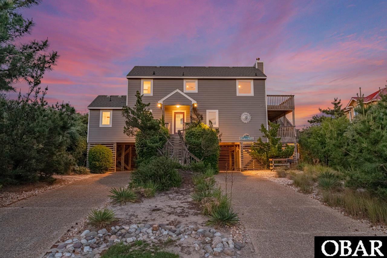 This 5 bedroom 3 bath "fisherman's" cottage sits on one of the most protective dunes in Ocean Hill or Villages at Ocean Hill. Stabilized with sturdy Russian Olives providing extra shelter from high winds and nor'easters. One, of only two homeowners, who have lovingly maintained this charming reverse floor plan. Offering an open concept, with stunning ocean views, and easy to clean ceramic tile throughout. The top-level boasts vaulted ceiling, juniper accents, a newer gas fireplace (2017), a large kitchen, dining area and huge primary bedroom with an ensuite bath. The great room has an abundance of windows providing lots of natural light and impressive views of the Currituck Lighthouse and the Ocean. The chef's kitchen includes ample counter space and cabinet storage, smooth-top range/oven, refrigerator, and a beverage fridge. Just off the great room is a wrap around porch, 3 sliders to an outstanding screen porch offering plenty of shade in the middle of the hot summer, and stairs to the mid and ground level. The spacious primary bedroom has an amazing view of the 4 wheel drive area to the north, and the ocean. There's also a private bath and private access to the screen porch. The mid-level has 4 more bedrooms, also with a private access to the covered deck, and 2 full baths. The exterior features low maintenance Hardiplank siding, a large owner's storage closet, outdoor shower, and an outdoor utility room. There's also a private walkway to the beach that sellers do not use. A buyer will need to add stairs should they choose. There's an estimate on file from Emanuelson and Dad. Home sits high and is an X-Flood Zone-no flood insurance required. The community beach access is three doors to the south, and should a buyer choose to join Villages at Ocean Hill amenities their oceanfront pool is just a short walk to the the north. Recent Upgrades include Simonton Windows installed in 2017, all polybutalene plumbing replaced, septic replaced in 2002, and more. Please see associated docs for the complete list. Ocean Hill is quiet and away from the hustle and bustle of tourist traffic. It's one of Corolla’s last paved communities before the 4×4 beach area. Buyers can join the Villages at Ocean Hill amenities (fee based) which include two community pools (oceanfront and lakefront), tennis courts, basketball courts, playground, fitness center and a 10 acre lake for fishing. This home is a perfect primary, secondary, or rental. Please see projection on file.