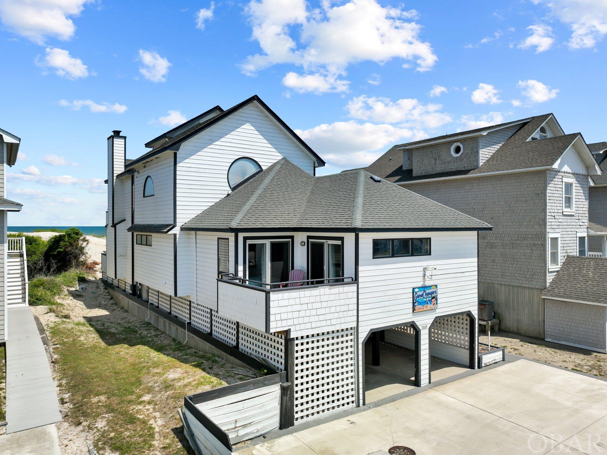 With an incredible $225K remodel done this offseason, get ready to be wowed by this oceanfront stunner.  Showing as one of the best in one of the most desirable locations on our beach not far from the legendary Millionaires row of Nags Head.  With six well-appointed bedrooms, this home has plenty of space to make memories with the entire family. The two top level masters offer additional privacy away from the other bedrooms and living spaces. The Ocean facing Master has breathtaking views with a private deck access. The west facing master offers another spacious sleeping quarter and has it’s own views of Jockey’s Ridge. The loft (very top level) has been repurposed into an arcade room that will keep the kids entertained for hours! The remaining four bedrooms are located on the main living area. With fresh flooring throughout and new TVs in all bedrooms, the bedrooms are set up for relaxation & rest after a long day at the beach. The renovated kitchen is perfect for entertaining and preparing meals with stainless appliances throughout. The kitchen area opens up to the main living space that has a fresh new look with updated decor, new furniture and reclaimed wood that shouts, "coastal chic." The wood burning fire-place is a favorite among all that visit whether it being friends, family or guest. Sporting a wet bar & a separate sitting space facing the ocean, this level of the home has something for everyone. With a new private walkway from the house to the beach, accessibility to the ocean is easy (for all ages). There is a clean, dry entry with plenty of parking for everyone.   Speaking of locale, "Game Changer" is located walking to some of the freshest seafood on the Outer Banks! Almost directly across from Jockey's Ridge, Kitty Hawk Kites and legendary Austin’s Seafood this spot is located in the heart of Nags Head and all the activities it has to offer. In fact, the local YMCA sits less than a mile away with indoor/outdoor pools, full weight room and complimentary passes for the remainder of 2023. Plain & simple, with it's location and recent upgrades, this home is set up for high ROI and is highly marketable for rentals due to those important factors.  Interior Upgrades: Whole house paint. New luxury vinyl tile floor.  Full kitchen upgrade with granite and new cabinetry as well as appliances.   New living and bedroom furniture.  New smart TVs. New LED lighting throughout. New window blinds & ceiling fans.  New Plumbing, New HVAC.   Upgrades: New Hot Tub, Driveway renovation, New Decks, Renovated Kitchen, Bedrooms and Bathrooms.  See Associated docs for full list.
