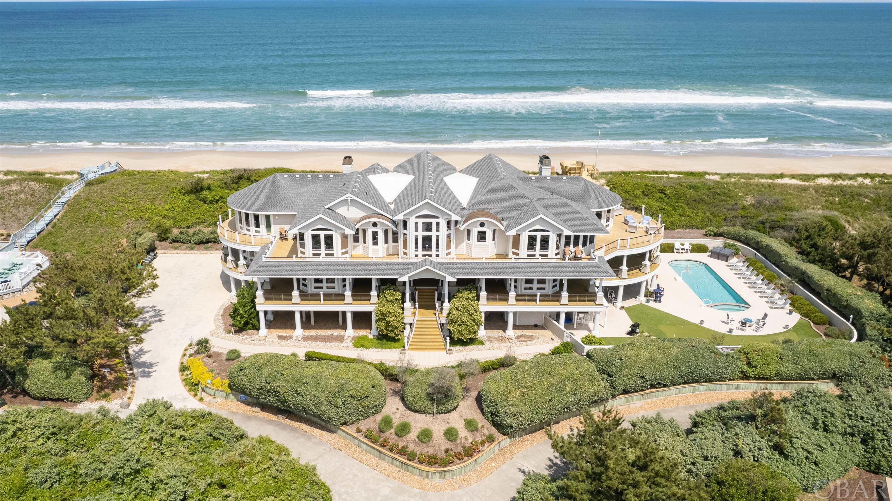 A WELCOME RESPITE - The OUTER BANKS PREMIER LUXURY OCEANFRONT ESTATE! In the picturesque northern Outer Banks where the Atlantic Ocean and Currituck Sound nearly unite, there is a stunning stretch of beach unlike any other, featuring a remarkable beachfront home unlike any other. With panoramic 360 degree water views, unobstructed sunrise and sunset vistas and 250 feet of secluded beach, this is your incomparable coastal retreat in the prestigious, highly desirable community of Pine Island. Nestled in Corolla close to the village of Duck but seemingly in a world all its own, the home’s nine bedrooms coupled with generous indoor and outdoor amenities, can be your luxurious private residence or a highly distinctive, coveted rental property. Each of the nine oversized bedrooms comes with an ensuite bathroom and spacious closets to accommodate plenty of family and friends. The bedrooms are spread across three floors -two on the first, five on the second and two on the third.  Inside and outside the 11,000 square foot home, a number of recent improvements and upgrades were made including newly refinished hardwood floors; new hardwood floors in the second floor hallway; new carpet in the theater room and in second floor bedrooms; new quartz countertops in the kitchen and wet bar; a new above ground hot tub; new third floor decking; new dune walk and deck; and much more. The remarkable living area is an open-concept floor plan with an expansive great room featuring huge windows overlooking the ocean plus a sizable dining room overlooking the Sound, and a thoughtfully designed gourmet kitchen with dual ovens, two dishwashers and three full-sized refrigerators. More benefits of the living space include: a home theater room that seats more than 10;two gas fireplaces;large,private office, a sauna with room for six; a rec room with a pool table, foosball table and table shuffleboard; a sun room; an elevator to easily move between floors; and a spacious one-car garage. Here in this self-contained oasis enjoy the invigorating, mild Outer Banks coastal weather on the modern cable-railed decks that wrap around the home for 360 degrees of unobstructed views. Just below the decks sits a pristine salt water pool and poolside wet bar complete with a refrigerator, sink and television. Also outdoors is a private five-hole putting green. For days when the sand and waves come calling, a private walkway provides special, direct access to a rarity on the Carolina coast - 250 feet of coastline. During cool nights, lounge around a luxury outdoor fire pit or enjoy a relaxing evening on the screened in porch. Every inch of the home is surrounded with professional, spectacular landscaping that effortlessly combines with the natural surroundings. Just outside the home is a semi-private street with just 2 other homes. Pine Island homeowners can enjoy the convenience of the private Pine Island airstrip. On the beach you may be lucky enough to encounter a sea turtle nest boil as the young turtles hatch and make their way to their ocean journey. On those days when you want to explore your neck of the woods, walk just across the street to a natural hidden treasure - the Pine Island Audubon Preserve. Here you can meander along a spectacular 2.5 mile nature trail filled with evergreen maritime forests of Loblolly Pine and twisted Live Oaks, stunted Oak forests and the rare Red Bay Shrub Swamp. Beside the shallow brackish water of the Currituck Sound, you’ll also enjoy a world filled with various wildlife and waterfowl. Nine miles to the north is the quaint village of Corolla with shops, restaurants, the historic Currituck Beach Lighthouse, the Whalehead Club, and the unique wild horse population. Just seven miles to the home’s south lies the award-winning Town of Duck. Exclusive, rare and spectacular, A Welcome Respite is the perfect retreat for those seeking privacy and adventure surrounded by unmatched natural beauty in the heart of North Carolina's Outer Banks.