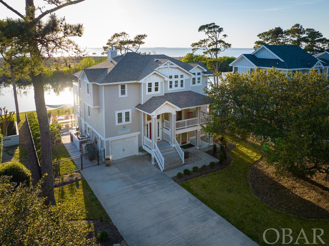 Welcome to Sand & Pearl. Built in 2016 by renowned OBX custom builder Dave Stormont, this beautiful 5-bedroom retreat is located in the heart of Corolla Light, a wonderful ocean to sound community in nestled in the live oaks surrounding Corolla Village. This home boasts breathtaking panoramic views of the sunset over The Currituck Sound, offering a serene and picturesque backdrop to your everyday life.  On the top level of this reverse floor plan home, you'll be greeted by a spacious and bright living area, perfect for relaxing, entertaining or just taking in the picturesque scenery overlooking the Currituck Sound. The open floor plan seamlessly connects the living room, dining area, and kitchen, providing ample space for your family and guests to mingle and enjoy each other's company. The kitchen is a chef's dream, complete with high-end appliances, custom cabinetry, and a large island with seating.  The home features 5 bedrooms each equipped with their own private bathroom, totaling 6 full bathrooms and 1 half bathroom, ensuring that everyone has plenty of space and privacy. The bedrooms are spacious and comfortable, offering a peaceful retreat at the end of a long day. The newly remodeled living space on the ground level is decked out with a NEW custom bar, making it the perfect spot for entertaining or relaxing with friends and family. Step outside through the sliding glass door and you'll find a private pool and newly fenced-in backyard overlooking the Currituck Sound, providing the perfect spot for outdoor gatherings. This home is also equipped with an elevator with ground level entry (no stairs to climb), making it easily accessible for everyone.  In addition to the amenities of this beautiful home, the Corolla Light community offers an array of activities and conveniences. Just a few of the highlights of this community are an indoor pool and sports complex, outdoor pools on the oceanfront and soundfront, a trolley service, and an oceanfront grill. Whether you're looking for a day of adventure or a relaxing afternoon by the pool, there's something for everyone in this wonderful community. This home has been METICULOUSLY maintained and functionally designed. It is only missing you! Don't miss this rare opportunity to own a soundfront home of this caliber in one of the most sought-after communities on the Outer Banks! More exterior pictures coming soon after new landscaping is completed.