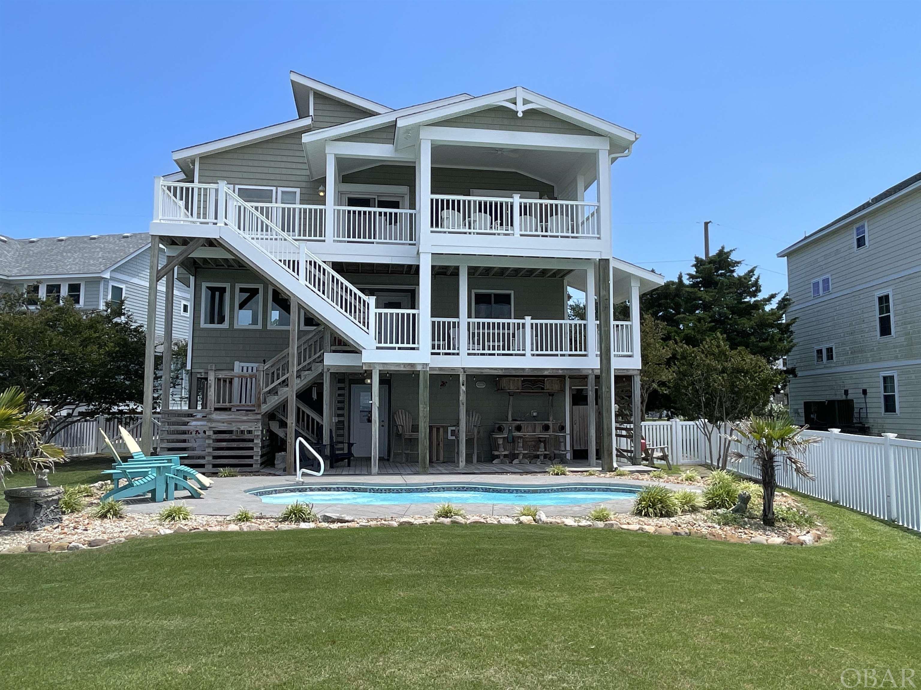 Welcome home to this stunning Sound front home featuring four bedrooms and two and a half baths with a saltwater pool and private pier. The spectacular panoramic view is as good as it gets in the OBX. Literally, food for your soul! Nestled on the serene Kitty Hawk Bay with easy access to the open waters of the Albemarle Sound this exceptional home offers a truly remarkable combination of luxurious living spaces. The home boasts an abundance of natural light with an open floor plan that seamlessly connects the living room, dining room and kitchen. High end finishes include granite counter tops, gas cook top, wall oven/ microwave with custom kitchen cabinets that offer ample storage. The center island offers additional countertop space for cooking prep and bar seating. The primary bedroom is on the upper level with a private bathroom featuring double sinks and a tiled shower. The lower level bedrooms are spacious, offering a serene space to rest and relax. The sunroom can double as an office or a cozy sitting space. The home also has a deep two-car garage with plenty of storage, hurricane shutters and two outdoor showers. Enjoy your private 210 ft pier for endless activities such as crabbing, fishing, bird watching, kayaking, paddle boarding, sunset viewing and star gazing. The pier was built in 2018 with ThruFlow Marine Decking. The open surface design protects against uplifting water and wind and hence is storm resistant and maintenance free. Hop on the one of the best multi use paths that OBX has to offer right at the end of your driveway.  Sold fully furnished with a small list of exclusions, this home is turn-key and move in ready!!  See associated docs for a full list of updates and the Bill of Sale with exclusions.