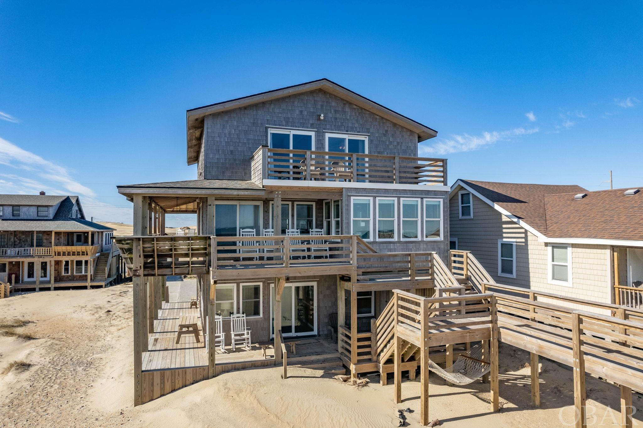 This indeed is a very rare opportunity for you to own in the unpainted aristocracy of Cottage Row in Nags Head. Listed on the National Register of Historic Places in the Old Nags Head District, this 7-bedroom, 6 full-bath home has been thoughtfully and intentionally upgraded without sacrificing any of its original charms. The traditional Nags Head Cottage design with wrap-around porches and abundant windows affords dazzling ocean views to the east and breathtaking sunsets over Jockey's Ridge to the west. Enjoy traditional style living on the open-concept main level with incredible views of the Atlantic and a nostalgic fireplace that beckons cozy, family gatherings. On the top level, you'll find four spacious bedrooms, two with en-suite baths and access to open decks for private sun tanning or ocean gazing, and two with a shared bath and incredible views of Jockey's Ridge. In 2019, three additional bedrooms and a den completed on the lower level with wet bar were added to this home. Outdoors you'll discover easy access to the beach, more seating areas and an outdoor shower. This property offers so much with its modern amenities while retaining its original Nags Head design. It's definitely a must-see!