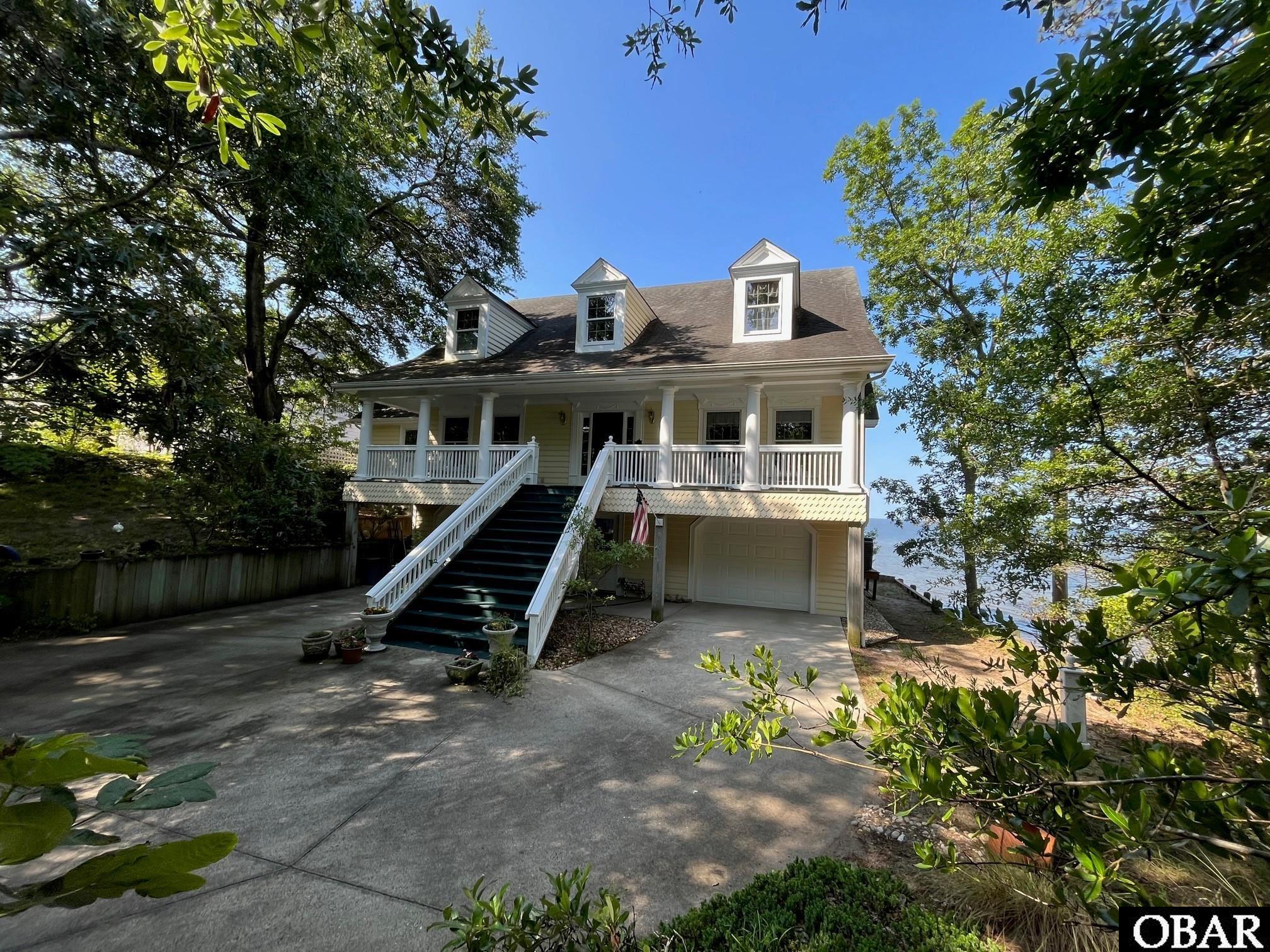 Beautiful custom Cape Cod style home with bulk-headed 82’ water frontage on the Albemarle Sound with southwest exposure...enjoy the spectacular Outer Banks sunsets and breezes!..high and dry sitting 15.5 feet above sea level! Quaint and quiet neighborhood in ideal central location...minutes to beaches stores and restaurants!..Upon entering the home you are greeted by a dramatic  two story foyer with chandelier . Living room with maple hardwood floors, family room custom wood mantle with gas fireplace, custom designed kitchen with solid maple cabinets and abundance of storage space, breakfast nook with wonderful sound views, classic dining room, ensuite bedroom with walk in closet, south facing 8'x30' sunroom, laundry room and a covered front porch are also included on this level. The top floor contains an loft living space with vaulted ceilings and a fireplace, 3 bedrooms, a full bathroom and finished 14' by 24' walk-in storage closet. On the ground level is an office or bonus space overlooking the sound, a full bath, two garages, and a 14' X 30' workshop or area for storage. Home was masterfully crafted by seller/contractor which shows in the details such as custom wood wainscoting, trim and crown molding throughout the home!..Bonus  Sound side sitting area...sits on a wooded homesite with well water irrigation system.  Two brand new (5/23) Goodman HVAC systems installed...Alot of home for the money and is an ideal primary, second home or retirement home!..worth taking a look and very east to show1