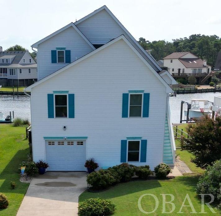 Location, Location, Location! The views will not disappoint and abound from this move in ready 4 bedroom 3 bath waterfront home. This home is the true example of a waterfront home that gives you numerous amenities to enjoy for all your watersport activities and outdoor living enjoyment.  Outside there is two piers plus the electric boat lift and a kayak launch platform with aluminum stairs into the water. The waterside yard is fenced in on 3 sides to keep your pets safe to enjoy their outdoor space as well. The screened in ground level patio has a custom built Tiki Bar with refrigerator and antique bowling alley floor countertop that is one of a kind. This outdoor living area is also host to a salt system jetted hot tub, propane fire pit and tv. Inside, there is plenty of room to entertain your guests with the open living floor plan and vaulted ceiling. There are 2 en-suite primary bedrooms, one on each level of this home. As well as 2 well appointed bedrooms and the third full bath. In addition, the open loft area on the second floor makes for a great small home office workspace and computer nook. The garage comes with a work bench area and prewired for a generator connection. Plus room for additional storage or a home gym. Recent Improvements include. Vinyl Bulkhead at the waterfront, Pella Energy Efficient Windows, HVAC, Water Heater, Kitchen Cabinets with Granite Countertops, Kitchen Appliances, New Carpet in Living Areas and Bedrooms. Custom Tile Shower with Glass Surround, LVP Flooring, Lighting, and Vanity with Marble Top in Primary Suite 1 Bath. The landscaped yard has a well supplied sprinkler system in place too. This waterfront gem is located in a gated boating community located on the Albemarle Sound at the Outer Banks of North Carolina. The deep water harbor has a dredged channel that leads to the Albemarle Sound and numerous waterways for ease of boating access to the Atlantic Ocean. Community Ammenities include 24/7 Guarded community entrance, Soundside Beach, Playground, Park with Pavillion, Boardwalks, Dog Park, Boat Docks, Bath House, Boat Launch Access, Basketball Court all included with the very low annual HOA fee. Clubhouse, Tennis Court, and Outdoor Pool access is offered with additional membership to the Colington Harbour Yacht & Racquet Club at an additional $250 a year. Security system in place with active video and audio recordings.