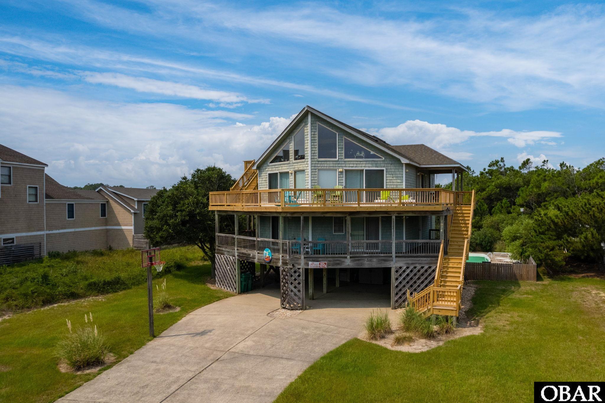 Welcome to Cowabunga! Your perfect beachside getaway awaits. This spacious semi-oceanfront property offers everything you need for an unforgettable vacation. Located just steps away from the beach, you'll enjoy stunning ocean views from the top-level deck, including a crow's nest deck with a view of The Currituck Lighthouse.  Relax on the wraparound decks, take advantage of the screened porch with a picnic table for al fresco dining, and soak up the sun. Inside, the top level features a beautifully designed great room with large windows, a gas fireplace, and easy deck access. The updated kitchen includes two dishwashers and stainless steel appliances, and cambria countertops making meal prep a breeze. The primary bedroom on this level accommodates a king bed and private full bathroom with walk-in shower. Up the stairs from the living area, is a fun loft space with sleeper sofa.   The mid-level offers two spacious en-suites and two additional bedrooms with a shared bath. You can unwind in the hot tub on the exterior decking or lounge in the hammock while enjoying the views and sea breeze. On the ground level, there's a rec room and an additional bedroom with a full bath.  Outdoors, you'll find a fully gated private pool area, charcoal grills, a volleyball court, and a carport with two enclosed outdoor showers. Cowabunga! has everything you need for a fantastic vacation. Jump right in and enjoy this amazing opportunity in the sought after Whalehead Community!