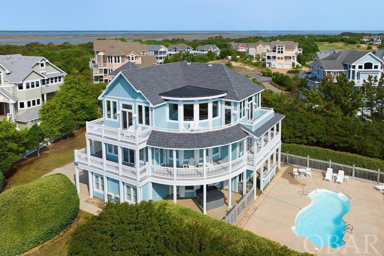 This spectacular home on one of the highest lots in the northern outer banks is a true gem, offering breathtaking views of the sound, ocean, and golf course. With 6 bedrooms and 4.5 bathrooms, a game room, and private pool, it provides the perfect space for to make memories on the Outer Banks.    Nicely appointed bedrooms with new carpet, amazing natural light and beautiful baths make for a welcoming retreat.  The master bath features a large tile shower and a free standing claw foot tub.  The top level, completely surrounded by new windows, doors, flooring and select furnishings, has plenty of space for gathering and relaxing or for a more private space up just a few stairs to a beautiful oasis to enjoy.  The views from the east and west decks cannot be matched!  Also on the top level, enjoy a large kitchen, with granite counters, great appliances, a wall oven and two dishwashers. Did I mention the huge breakfast bar with plenty of room for six?  Need to get away? The game room is the perfect spot for some friendly competition, while the private pool offers a refreshing retreat from the summer heat. Easily accessed from the game room the pool is just outside.  With the recent addition of a shaded bar area, the choice of sun or shade is yours while still enjoying the outdoors and the beautiful landscaping this home offers.  If you're looking for an investment opportunity, recent updates have increased the 2023 by more than 20%.  This rental machine can be yours!  Recent updates include the roof, siding, interior and exterior paint, and windows and doors on the top floor.  You can be certain that this home is not only beautiful but also well-maintained. Ask about the full list of recent updates.  Whether you are lounging on the deck, taking a dip in the pool, or simply enjoying the panoramic views, this home is the ultimate beach getaway. With its prime location and luxurious amenities, it is the perfect choice for those seeking a truly unforgettable home.
