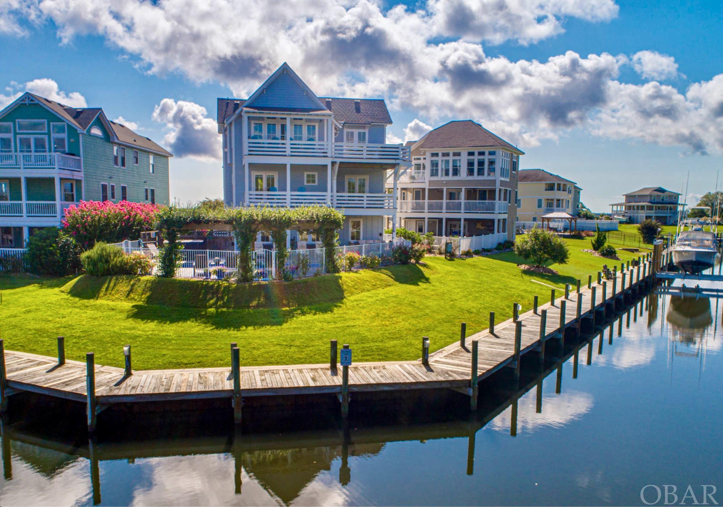 Experience coastal luxury at its best with this stunning 5-bedroom, 4-bath waterfront haven in the esteemed boating enclave of The Peninsula, Outer Banks, NC. Set on a high lot with 140 feet of deep-water canal, this coastal gem offers a seamless blend of indoor-outdoor living, boasting breathtaking views of Shallowbag Bay and the tranquil marshland. Crafted by renowned OBX builder Mike York, this home is a masterpiece of craftsmanship and tranquility. Upon entering the second-floor main entry, you're greeted by Eddie Bauer engineered hardwood floors, intricate custom carpentry, and a tray-paneled accent ceiling crowned by transom windows. The open-concept design harmoniously marries elegance and functionality, offering an inviting living experience. Ascend to the top level via elevator or stairs to discover a captivating realm of custom details, characterized by soothing sea-toned palettes. The expansive great room features a gas fireplace with a bespoke mantle, vaulted ceilings adorned with handcrafted wood beams, and transom windows that frame the panoramic views. The gourmet kitchen is a chef's dream, boasting leathered granite countertops, 48” KitchenAid gas cooktop, double electric oven, and handcrafted light fixtures crafted from California wine barrel rings. The mid level is home to three bedrooms, two of which offer private access to a spa-like Jack & Jill bathroom with Caribbean marble countertops and vessel sinks. The main primary suite boasts a luxurious bathroom with a double vanity and a custom tile shower with dual rain shower heads. This level also hosts a utility room with washer/dryer and ample storage. On the ground level, find another king-sized bedroom, a full bath with Caribbean marble countertop, and a tastefully designed entertainment space featuring inlaid tray ceilings, pool table, multiple large-screen TVs, and a wet bar. The outdoor space is an oasis of relaxation, showcasing a saltwater pool, 7-person hot tub, and a spacious gathering area under a charming trellis adorned with fragrant Jasmine. Additional amenities include a one-car garage with laundry facilities and storage, Hardiplank siding, and a room for pool equipment. The Peninsula community offers hassle-free yard maintenance, a community boat ramp, and an ideal blend of second-home and primary residences. Don't miss this opportunity to embrace waterfront living in its finest form. Your coastal dream home awaits.