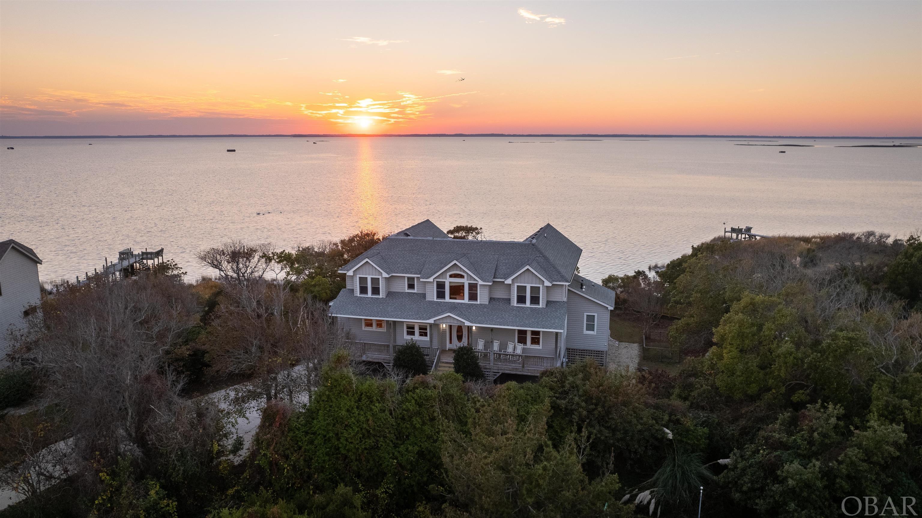 Enjoy coastal living at its finest with unobstructed water views over the Currituck Sound in this well appointed and ultra private Sanderling home.  This stunning custom home built by Ken Green checks all the 'waterfront dream home' boxes situated on over 1/2 acre at the end of a quiet cul-de-sac with a private pier, kayak launch and endless sunsets on the expansive sun and covered decks.  As you walk into the foyer you are greeted by a wall of windows capturing endless water views from every angle.  The main level boasts a gourmet kitchen with a large breakfast bar, Hi-Macs solid surface countertops, dual sinks, built-in cooktop and double ovens, and a dining area and great room offering plenty of space to entertain all while overlooking the gorgeous sound vistas.  You will also find a large private office, the perfect space to work from home and also permitted for a 6th Bedroom, a powder room, laundry room, sunset viewing sunroom (with separate mini split), and a 1st floor King primary bedroom with more sound views. Upstairs boasts 4 additional bedroom suites with stunning picture windows and water views, all with private en suite baths, a loft style den/sitting area, a 2nd stacked full size washer/dryer, and a sun deck to take in even more sound views.  Built with timeless details and amenities including an Elevator, Central Vac, surround sound speaker system, solid interior doors, hardwood flooring, gas fireplace, Juniper tongue and groove walls throughout (even more stunning in person!), and cedar lined closets, this home is both comfortable and grande and makes the perfect place to call your Outer Banks home.  The ground level offers tons of storage options inside and outside, as well as covered carport space for 3 vehicles.  Outside you will enjoy ample side and backyard space for outdoor entertaining, beautiful landscaping with irrigation including fig trees by the front entrance, a garden area and an outside shower.  The private pier has brand new light and rope and is ideal for kayaking, crabbing, fishing, swimming and sunset watching!  The Sanderling community in Duck offers a Soundfront community pool, racquet / health club and tennis courts, and boasts about a mile of uncrowded beaches, and serene nature paths.  All just a short distance north of the quaint town of Duck known for its incredible shopping, waterfront boardwalk and restaurants!