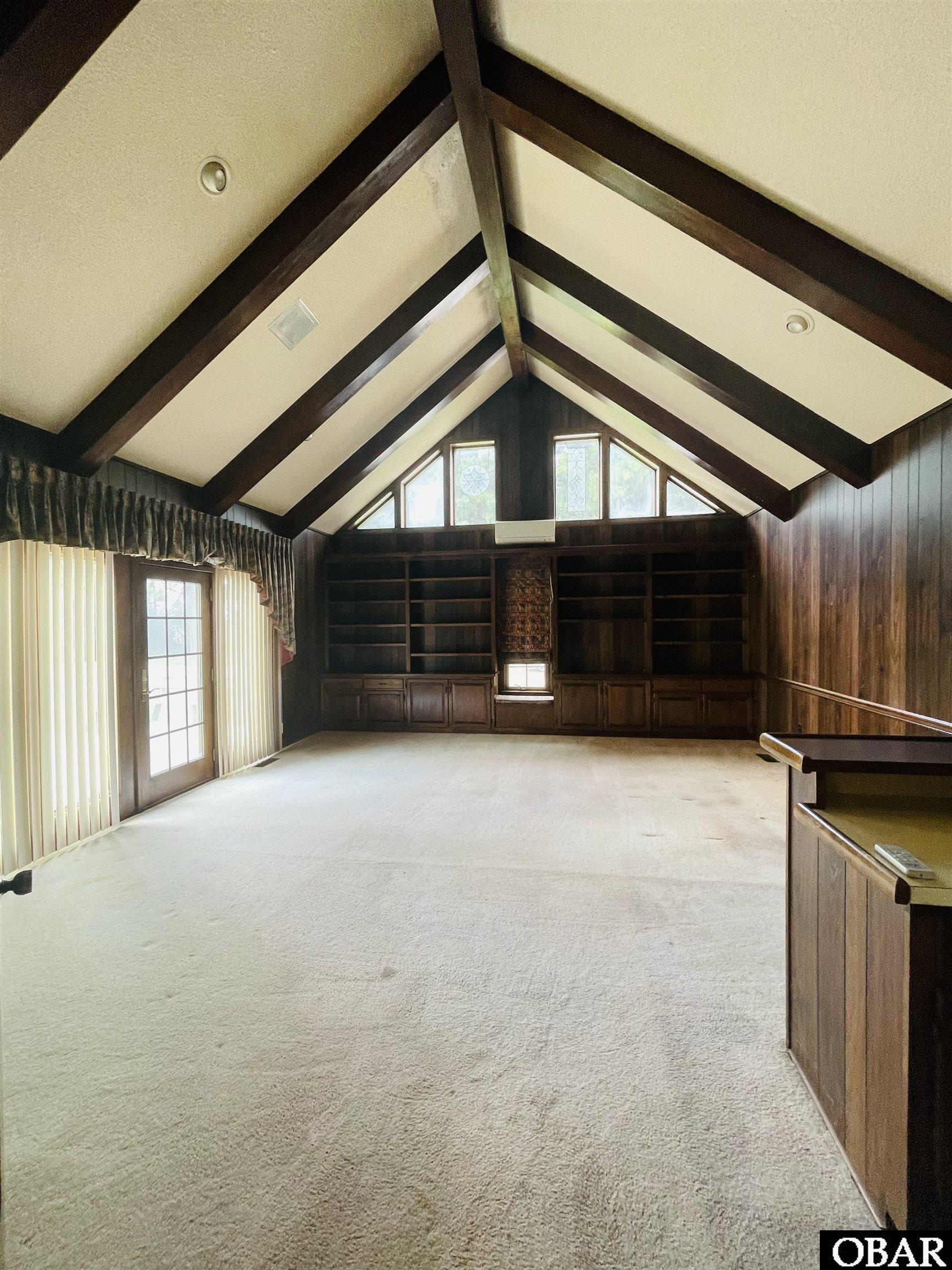 Handsome den w/ cathedral ceiling, beams, built-ins, bar, and patio doors to deck. Right off kitchen.