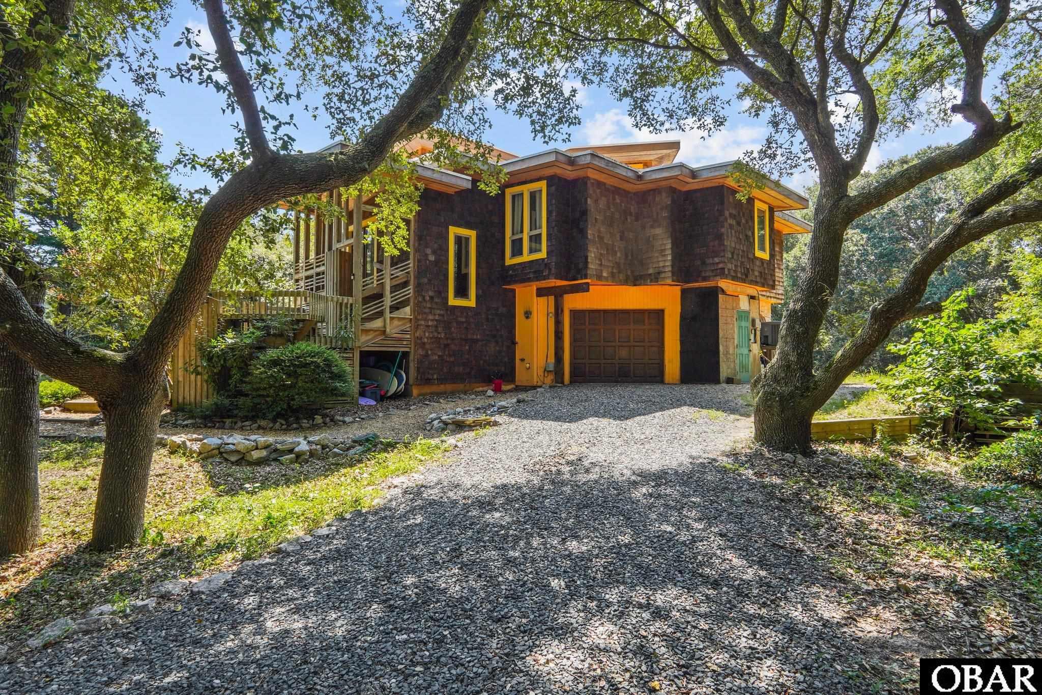 315 Duck Road Sellers are offering $10,000 Credit to Buyer at Settlement for Contract Ratified Prior to December 31, 2023! This remarkable treehouse exemplifies rectilinear architecture, nodding to Frank Lloyd Wright while folding in the historical style of Outer Bank's legendary developers Frank and David Stick.  Designed to blend into the trees with an added pop of color, this 3 bedroom, 2 bath is tucked onto a naturalized Southern Shores 35,000 sq foot lot.  The two story flattop has a TPO (Thermoplastic Polyolefin) roof less than 3 years old with 12" waxed mahogany fascia with large cedar soffit overhang.  The cantilevered reverse floor plan features a top level en-suite with covered screened in porch.  Heritage oiled cedar shakes envelop the exterior while custom woodwork and hand painted murals grace the inside.   A private salt water swimming pool and custom covered Tiki Bar offer a place to hang out after longs days of surf and sand. A Southern Shores private Atlantic Ocean beach access is at end of 7th Avenue and is less than a quarter mile away.   Unique features of the home include a water forced hot Air Handler (less than 5 years old) and AC Compressor, ground level radiant floor, a second kitchen on ground level to compliment the 2nd and 3rd bedroom, a one car garage and plenty of parking on the gravel driveway.  As Southern Shores is a segue to Kitty Hawk and Duck and very close to restaurants and shopping, the location does not disappoint! Build your investment portfolio or keep this wooded haven to yourself and enjoy all the Outer Banks has to offer!  The pool has been re-plumbed and house has pex water lines and PVC drains. Video Walkthru:  https://youtu.be/ROdik6F1S2A?si=i5aPTejhujtlo1KG