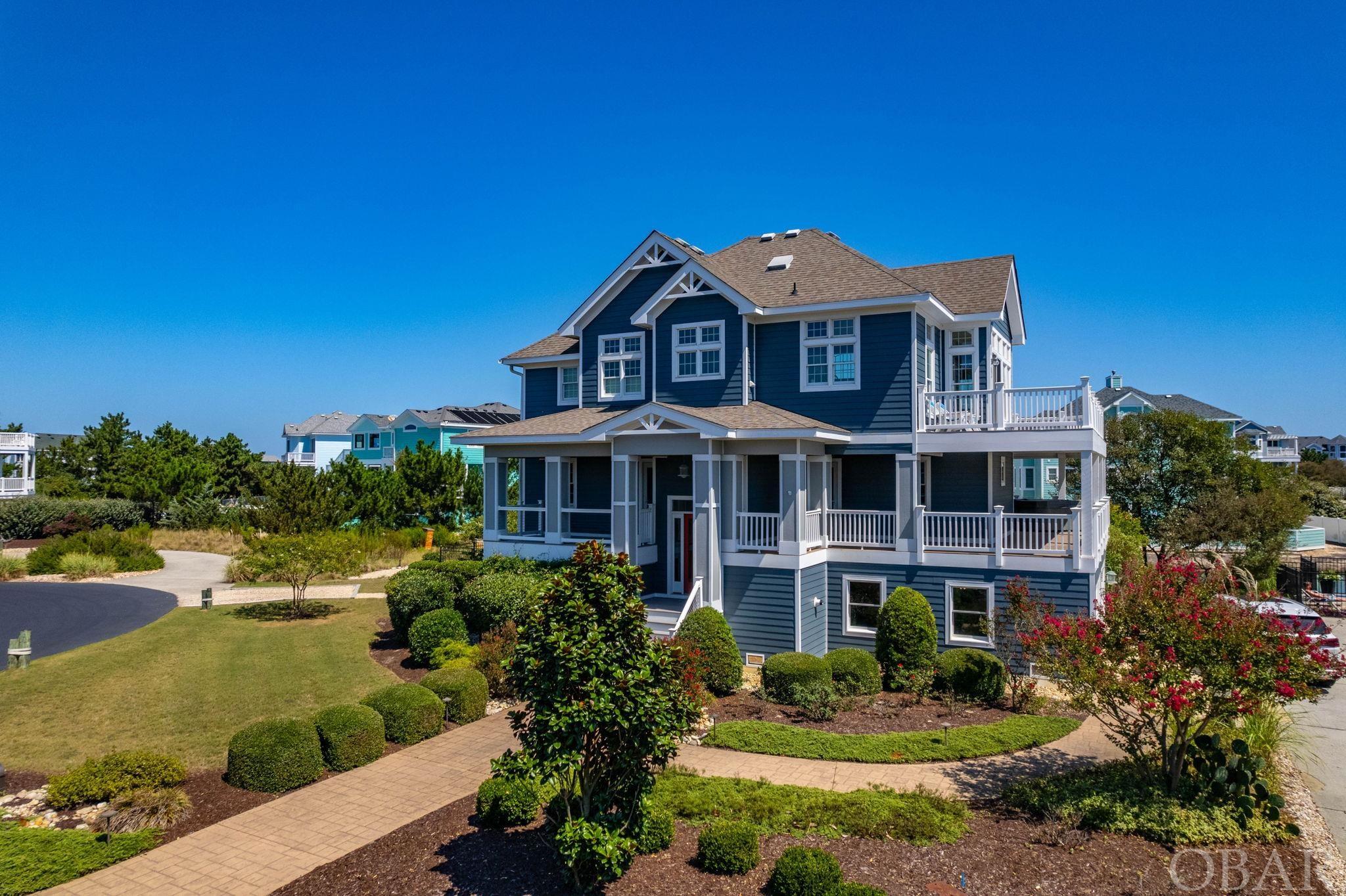 Located on a cul-de-sac, this remarkable 4-bedroom, 4-bathroom Buck Island property invites you to experience the pinnacle of coastal luxury. Situated in an 'X' flood zone, this home showcases high end finishes and a wealth of amenities for those in search of the Outer Banks lifestyle. The beautifully landscaped lot sets the stage for the grandeur that awaits within. Meticulous care has been taken to create a lush, welcoming environment that enhances the overall aesthetic of this private second home. Inside, discover the top-level, where natural light streams in from a panorama of large, mullioned windows encompassing the family room and dining areas, creating an inviting atmosphere. A gas fireplace provides cozy ambiance, and the cathedral ceiling and warm natural hardwood floors present an open airy feel to this space. From here, access the top deck to savor subtle ocean views that offer a tantalizing glimpse of the Atlantic in addition to the pond and fountain below.The kitchen, a chef's dream, is equipped with top-tier stainless steel appliances- Viking gas stove, wall oven, microwave, refrigerator, as well as a Bosch dishwasher. This culinary oasis also features sleek black natural stone countertops complimented by white subway tile and a breakfast bar workspace complete with power outlets.  Custom cabinetry, a high ceiling, and natural light from the mullioned windows add to this culinary haven. The top floor also boasts the spacious main en suite bedroom with private balcony. The large en suite bathroom enjoys natural light and features a double vanity, jet tub, and custom tiled glass front shower. This retreat is designed for ultimate relaxation and privacy. (A powder room between the upper and middle floors offers convenience for all.) The middle floor boasts another elegant en suite bedroom, 2 additional guestrooms, and a shared full hall bathroom, providing flexibility for families or guests, ensuring comfort and privacy. The practicality of daily life is made effortless with a dedicated laundry area on this floor, and an outdoor hot tub located on the expansive mid deck provides a relaxing, shaded escape to be enjoyed year-round. The ground-level den, complete with a wet bar and full size refrigerator, serves as the ideal hub for cozy movie marathons and could accommodate a regulation size billiard table. A full bath with custom tiled shower on this level provides convenient access to both the den and private pool just steps away. Discover your own private outdoor retreat - a glistening pool with expansive custom decking, an alfresco kitchen with granite counter space and a built-in gas grill, and a captivating fire pit beckon, promising countless evenings of enjoyment and relaxation. This Buck Island gem not only offers convenience to local restaurants, shopping, and attractions, owners in this premiere oceanside community enjoy amenities such as dedicated ocean access, community pool, and tennis courts. This coastal sanctuary is more than just a second home, this property is an invitation to embrace the Outer Banks lifestyle.