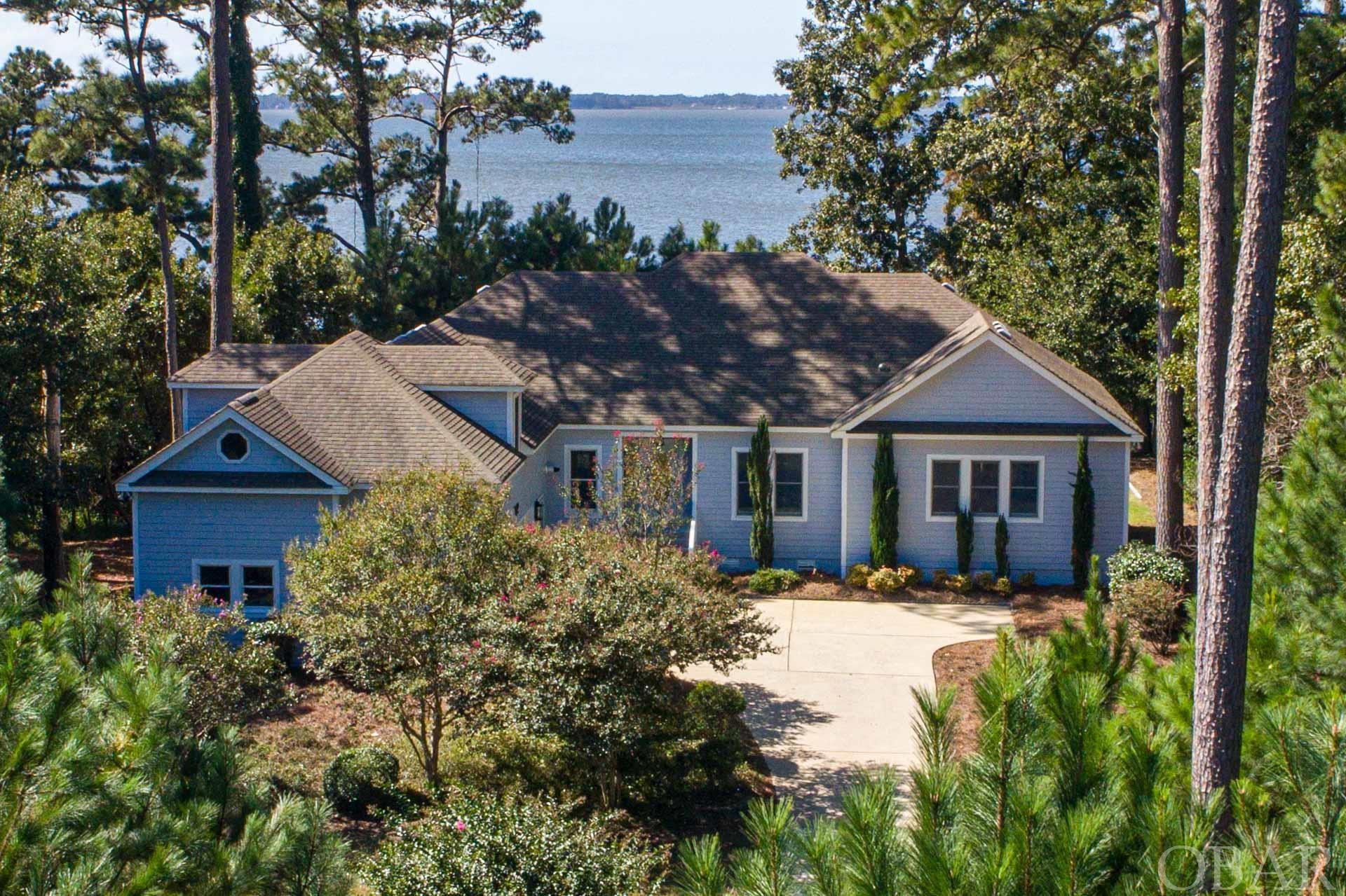 Experience instant tranquility as sunsets grace the waters of this beautifully-maintained coastal home in Martin's Point. Nestled within the sought-after gated community of Martin's Point on the Outer Banks, large parcel (33,500 sq. ft.) offers a serene oasis on the picturesque Currituck Sound. Constructed By renowned OBX Builder Waldt Construction, and gently loved by original owner. As you step into the chandelier-graced vaulted foyer, the Great Room's wall of windows showcases sensational water views, setting the tone for elegant living spaces throughout. The living spaces flow effortlessly, including a formal dining room, a charming home office/library with plantation shutters and custom built-ins, and an open-concept kitchen with informal dining spaces that exude the heart of the home. This single-floor residence (except for Bonus Room) boasts cathedral ceilings, gleaming hardwood floors throughout, 9' ceilings, and a cozy gas fireplace that heats the home extremely well while creating a warm and inviting atmosphere. The chef's kitchen, complemented by a neutral palate, overlooks the pool and the stunning Currituck sound. Offering a gas countertop range, solid surface countertops, loads of cabinetry for extra storage, a disposal, pantry, and center island. A conveniently located rear door off the kitchen and sliders off the great room will take you straight the the gas grill and large sundeck with automatic remote control awning. A great place to watch the children in the pool or be captivated by those famous outer banks sunsets. The generous primary suite features plantation shutters, a gas fireplace with granite surround, amazing water views, and a newly renovated private bath with tile flooring, walk-in tub, double vanity, and separate custom tile shower adorned in soothing colors. Also included in this oversized suite are two ample-size walk-in closets. There are two more spacious bedrooms bedroom each with their own private access to a full bath. One of the bedrooms overlooks the sound and the pool, and has gorgeous custom plantation shutters. Conveniently located off the two car garage is the utility room, with a laundry sink, washer, dryer, and custom shelving. Over the garage is an enormous flex space with a wet bar and mini-fridge. Enjoy tons of storage in this room with a floored attic, and plenty of alcove storage. This area is the perfect space for a game room, media room, or potential to turn into a 4th primary suite, by upgrading the septic and adding a private bath. Discover unique nooks and niches throughout the house, perfect for savoring morning coffee or evening beverages. From the quaint sound-front covered gazebo, the huge sun deck off the great room/kitchen, large pool area, and private pier – you'll have ample spaces to enjoy breathtaking sunsets, crab, launch kayaks and observe lots of wildlife in their natural habitat. The exterior offers a saltwater-solar heated pool, irrigation system in front and back yard operated with an app, natural gas serves fireplace, grill, water heaters (tankless), countertop range, and dryer. Martin’s Point amenities offer 24/7 security at the gated entrance, a private marina with boat ramp and slips, multiple stocked fish ponds, playgrounds, and a waterfront pavilion for hosting gatherings. Additionally, you can take advantage of the yacht club membership and participate in a variety of coastal activities, such as kayak outings, sailboat racing, holiday decor contests, and more.