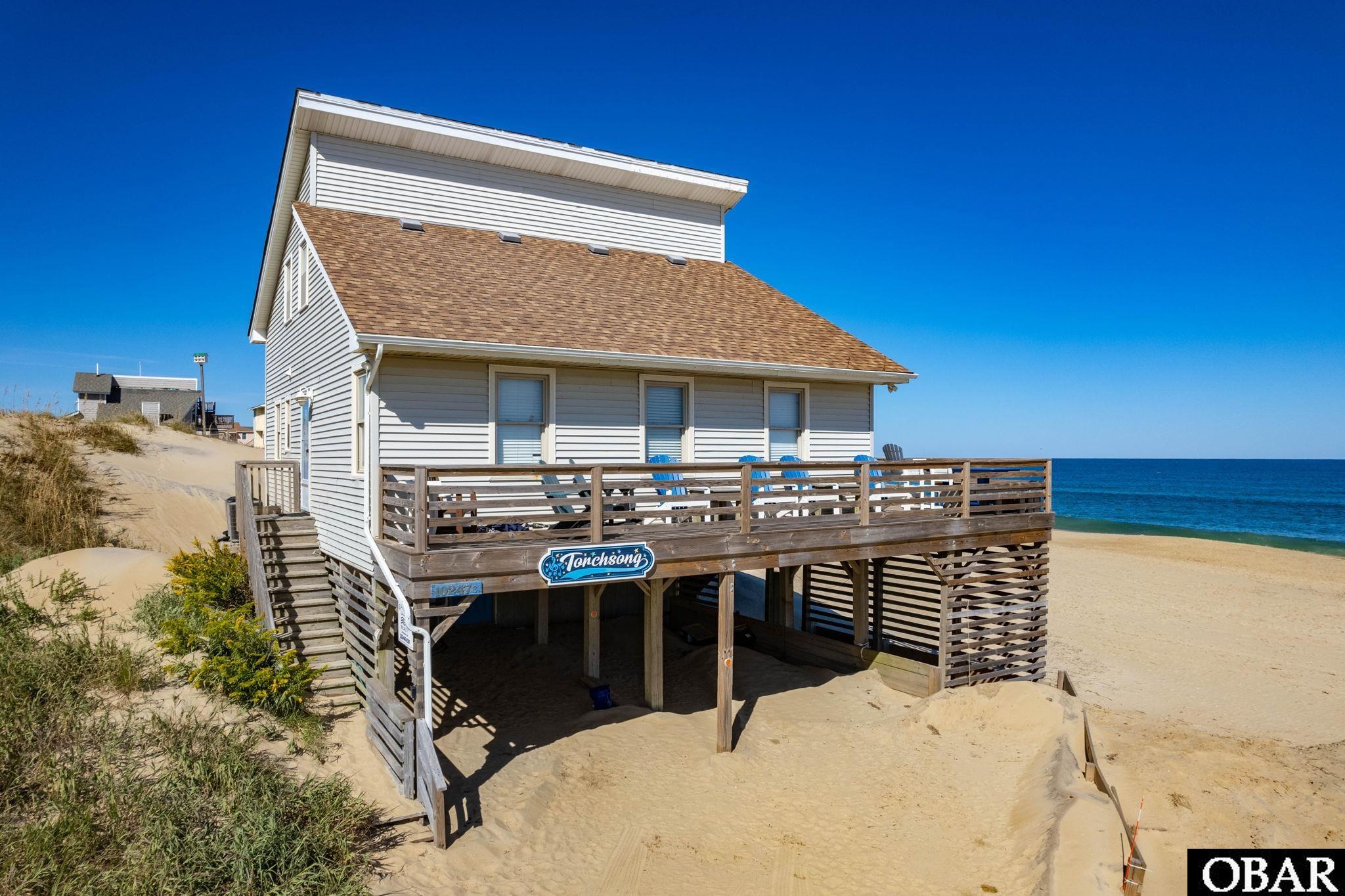 Be prepared to have your socks knocked off, this oceanfront Salt Box has consistently produced over 10% in gross rental income the past three years! Add back in the weeks the owners enjoyed in 2023, the gross rental income generated equals $90K!!! What a fantastic return and the online reviews show how the guests appreciate the well-stocked kitchen and many comfortable seating for their guests. Torchsong is well named and a winner! Where do I start? The gorgeous views of the Atlantic Ocean, the beautiful beaches, the wide two-sided decks with generous seating, the awesome great room’s open layout and abundant natural light, the cozy seating for gatherings around the electric fireplace for a chat. Like the mermaid's song, Torchsong will charm you with it's easy going and warm atmosphere enhanced by the aged juniper ceilings, you will find generous size bedrooms and so many improvements made throughout these past four years. The lower level was refurbished with a new vapor barrier, new plywood flooring and underpinning and offers ample room to store the beach toys and house the washer/dryer, air handler, water heater and owner’s locked storage and, the convenience of an outdoor shower to wash off the sand. Torchsong has been outfitted with new furnishings and dining set, bedding and comforters, blinds, new flooring, kitchenware (the works!), art work, adorable and sturdy bunk beds. The list is long and available. The large ticket items are: roof replaced in ’19, stronger siding material installed on entire east wall, new decks w built in bench, stairs & landing ’20, two new bulk heads ’21-‘22, two new heat pump systems ’22, refurbished subflooring and new luxury vinyl flooring on main level, all new Polywood chairs, tables, and picnic table.  All this in the fabulous location of South Nags Head, the home of the historic Whalebone Junction, Sam & Omie's Restaurant, Jennette's Pier, and the Outer Banks Fishing Pier. With several miles of gorgeous beaches and sidewalks, this could be your paradise. Are you ready?