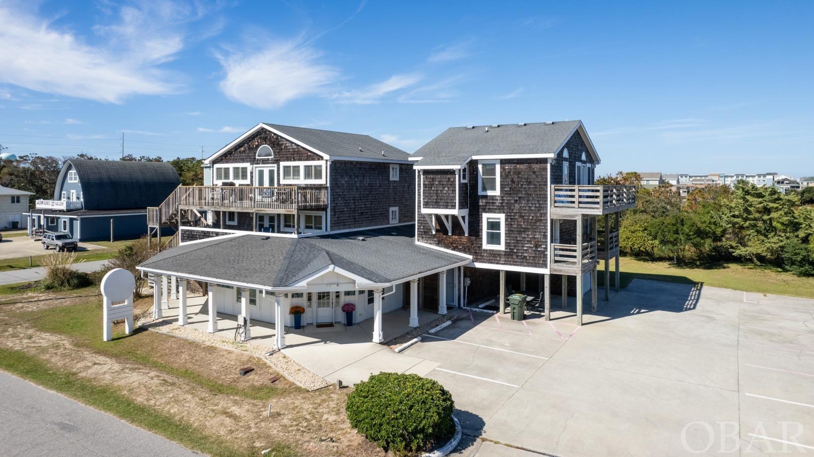 INVESTMENT OPPORTUNITY!!  Discover the allure of this exceptional property featuring two distinct 4-bedroom residences accompanied by versatile commercial space in the coveted Gallery Row District in Nags Head.  Situated on 2 full lots, this is a truly unique opportunity on the Outer Banks. Whether you choose to maximize rental potential across all three spaces, establish a live-work dynamic by residing in one unit while operating a business in the commercial space and renting the other unit, the possibilities are endless!  The east unit offers an upper-level great room inclusive of a primary bedroom with a generous walk-in closet and bath. The mid-level encompasses three additional bedrooms and two bathrooms, with laundry conveniently situated on the first level. The west unit is fully furnished and ready for guests! The top level offers a kitchen, living area, primary bedroom, and a bonus room along with a full hall bath. The mid-level hosts three more bedrooms, two baths, a secondary living space complete w/ a mini-theatre set up, foosball, and laundry.  Both units seamlessly integrate outdoor living with expansive decks offering a bit of an ocean view and a great place to relax. An outdoor shower adds a necessary convenience for you and your guests. The commercial space on the ground level offers an open floor plan, ample storage, a half bath and parking for up to 15 vehicles.  Perfectly positioned just three lots from the beach, this property is within walking distance to local gems like Red Drum and just a very short drive to Kill Devil Grill and Swells'a Brewing Company.  Not to mention you are in the heart of Gallery Row where you can stroll through the galleries and shops of local artists like the Glenn Eure Gallery and Seagreen Gallery.  It's just an awesome location!  Immerse yourself in the possibilities of this amazing property!