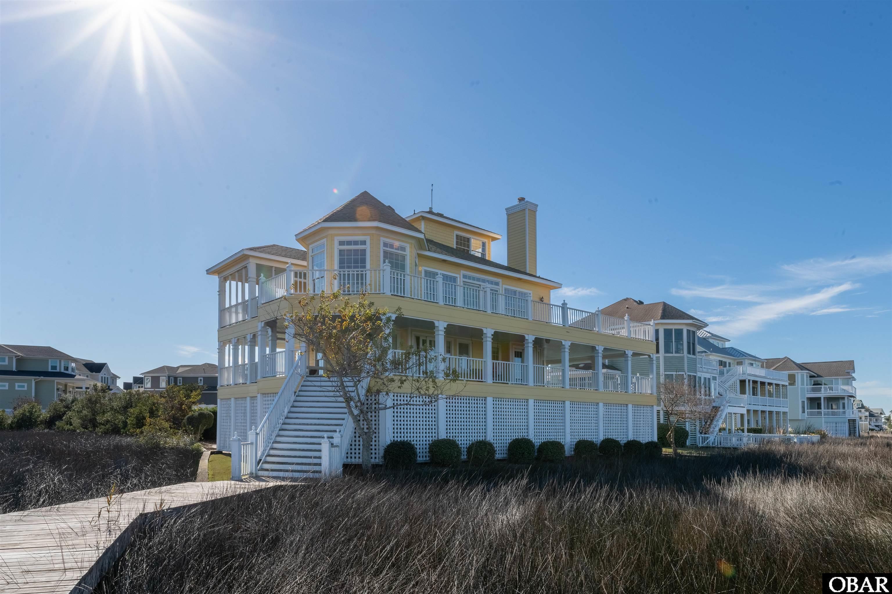 Location, Location, Location!!!!! This 4-bedroom, 3-bathroom residence stands out for it's exceptional location on one of the choice lots in Pirate's Cove with 270+ degree views.. Upon approaching the long driveway, you'll be captivated by the enchanting garden and gazebo, with sitting area. The reverse floor plan of this residence offers a genuine home-away-from-home experience, providing stunning views of Pirate's Cove canals, the marsh, downtown Manteo and the sound. Prepare to be entranced by the breathtaking sunrises and sunsets that make this property truly remarkable. Upon stepping into the foyer, you will be instantly struck by the exceptional craftsmanship evident throughout this residence . The antique original Quarter Sawn Heart Pine floors throughout, coupled with the wood wainscoting and wood paneled ceilings, create a cozy and warm ambiance, adding to the over all charm of the home. Every closet and storage room is lined with rare Atlantic White Cedar. The first floor has three of the bedrooms, all with access to the back decks and the captivating views framed by detailed architectural trim and rare finished ceilings under the deck. Two of the bedrooms share a Jack-N-Jill bathroom. The other bedroom is the primary with ensuite. The main level will mesmerize you with the views from the expansive windows. The open concept kitchen, dining and living room, with wood burning fireplace, all have floor to ceiling windows. There is another guest room with ensuite and deck access. The top floor ships watch has 360 degree views. This area could be an office, bar or just a reading room,  the possibilities are endless.  There is so much deck space, everyone will have room too spread out. Ground level has plenty of parking, a dry entry, a two car carport  and  double outside showers, a shop and a gated area, perfect for your golf cart and all your beach toys. This is one of largest lots in Spinnaker Village, with beautiful manicured landscaping. There is a 55 foot boat slip that conveys to qualified boat owner for an annual fee of $160. Its prime location also provides quick and easy boat access to the sound. This was one of the first lots sold in Spinnaker Village- for good reason- making this a rare opportunity to acquire your dream home.