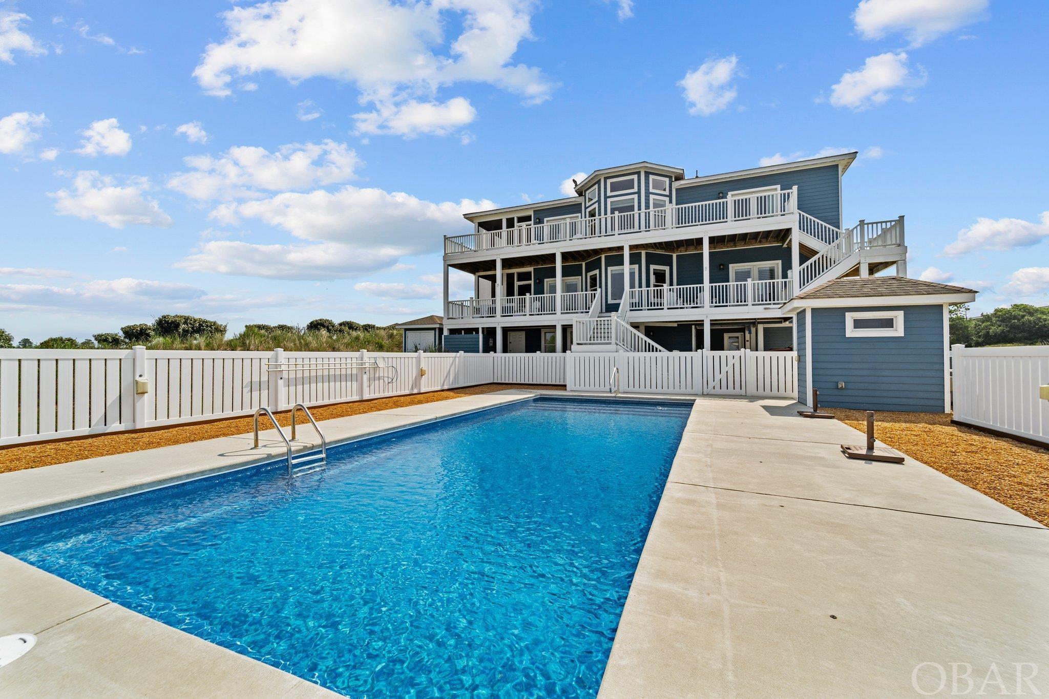 Always wanted to live on a golf course AND have panoramic Ocean AND golf course views? Pack your clubs, 303 Grissom Street in Kitty Hawk is the home for you. This 4,877sf home constructed in 2018 by Stan White Construction sits on a 20000sf lot in an X Flood zone lot and boasts a fenced in 16x38 lit saltwater pool with exquisite Ocean views. Beautifully landscaped and located on the 11th green. Exterior composite decking on all sides, East decks lead to every level of the home.    The lower level consists of a spacious area that can be used as a theater room or an entertainment/recreational room fully equipped wet bar, half bath with outside pool entry door. Off this area is the laundry area and 2 large bedrooms with a shared bathroom with tiled walk-in shower.      As you approach the second level hallway, there is a walk-in closet with shelving and plenty of storage.  Entering the 2nd level, this living space has a half bath. A fully equipped kitchen with subway backsplash and pantry (which was originally done for an alternate private space) for friends or family staying during the holidays. A dining area with bay windows and access to the screened porch with golf course and ocean views and access to East decking. A primary en-suite with extra-large walk-in tile shower with walk in closet and deck access and another primary bonus room with a tiled shower.    The third level has a full walk-in closet at entry and as you enter the main living area you have a fully equipped kitchen with a pantry and access to another screened porch off the living area. An en-suite with extra-large walk-in tile shower, a clawfoot tub and a private room with toilet and another primary bonus room with bathroom large tiled shower.    Notable features include elevator, 2 gas fireplaces on mid and upper levels, top of the line fixtures, Atlantic Quartz countertops, extra wide trim/molding around doorways, Levolor custom window treatments, LVT flooring throughout with carpeting on all interior steps.   Concrete walkway throughout the access areas of carport to the fenced in pool and outside shower area. An 8x24 storage building behind the home for even MORE storage. This home has excellent rental potential as an investment property, a lovely main residence or 2nd home.