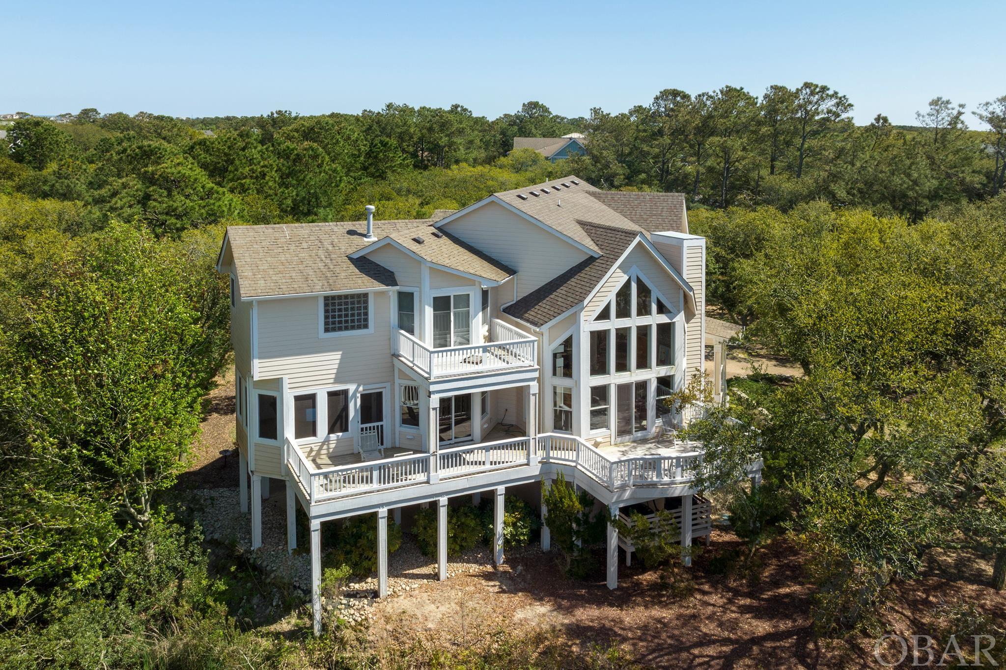 This semi-soundfront 5-bedroom, 4.5-bath residence (original owner and lovingly maintained) boasts a unique charm that sets it apart from other Outer Banks homes. The breathtaking vistas offered by this property are simply unparalleled. From the picturesque wooden bridge framing the tranquil Currituck Sound, to the west-facing wall adorned with cathedral windows that perfectly capture this serene scene, every aspect of this home exudes elegance and tranquility.  Nestled amongst majestic mature live oaks on a private lot, this residence stands as a tranquil haven. An elevator serves all three floors, ensuring convenience and accessibility. Upon stepping inside, you'll be transported to a world of serenity and sophistication.  The panoramic views from this property are truly awe-inspiring, showcasing both the enchanting sound and the meticulously designed Rees Jones Golf Course of The Currituck Club. Whether you're drawn to the captivating sunsets, the joys of birdwatching, or simply yearn for a place of relaxation, this home offers it all.  The main level features a delightful, updated kitchen and open living spaces strategically designed to maximize these breathtaking views. The expansive windows seamlessly blend the outdoor beauty with the indoor elegance, allowing you to savor every moment within this picturesque setting. The generously sized bedrooms ensure the utmost comfort.  Outside, the beauty of this property continues, offering ample space for sitting and immersing yourself in the great outdoors. If your dreams include a private pool oasis, you're in luck; the generous lot size can accommodate your vision.  This is an extraordinary opportunity to make this remarkable property your own, a rare combination of natural beauty, modern comfort, and endless possibilities. Don't let this Currituck Club gem slip through your fingers—schedule a visit today!