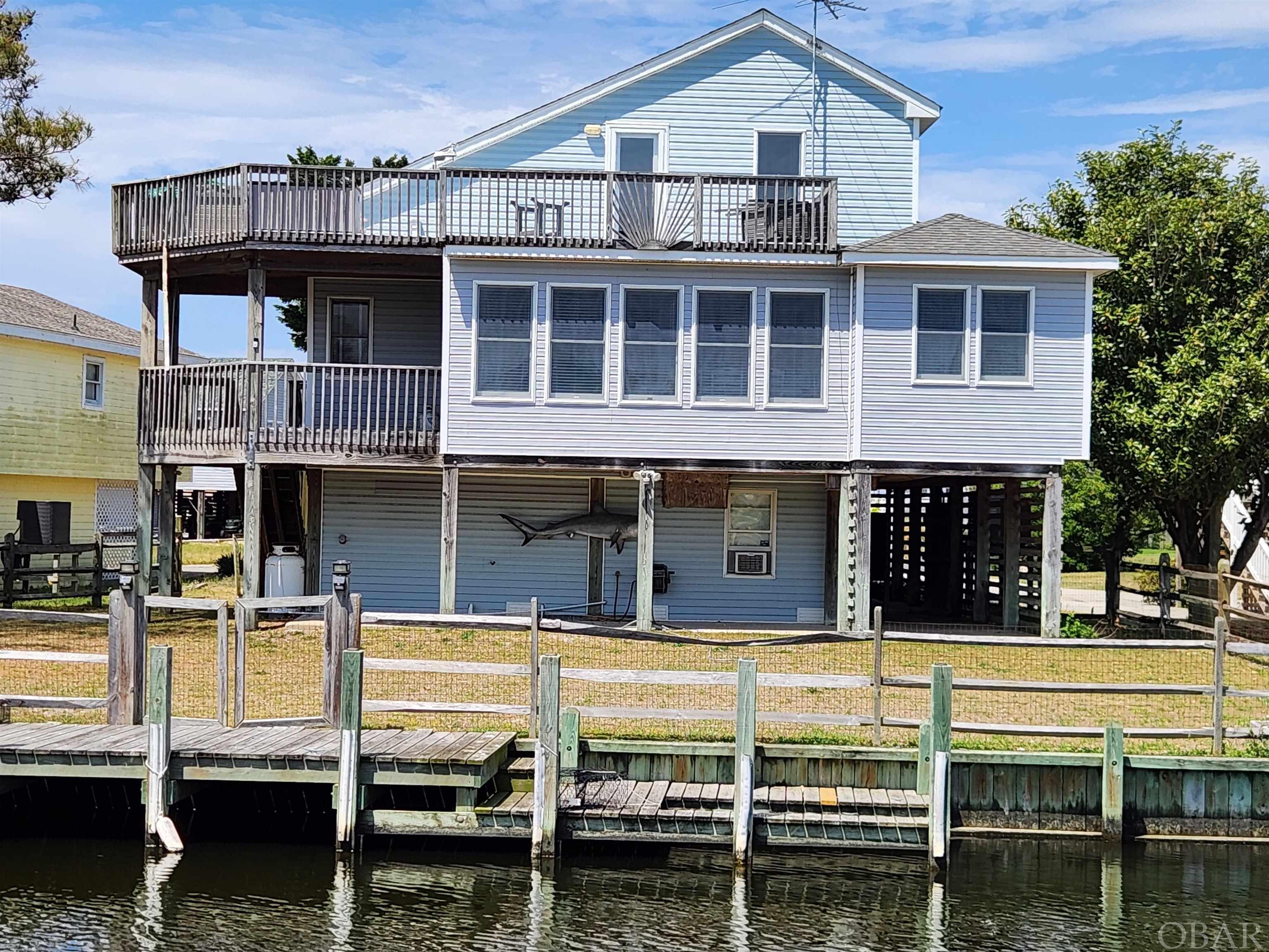 BOATERS!!! or ... WATER LOVERS! ... COLINGTON HARBOUR ... 75' ON DEEP WATER CANAL WITH DIRECT ACCESS TO THE SOUND! BULKHEAD IN PLACE WITH DOCK AND JET SKI / KAYAK LAUNCH! HOME FEATURES EXTENSIVE CANAL VIEWS AND SOUND VIEW *** ROOFTOP DECK WITH EXPANSIVE CANAL VIEWS AND SOUND VIEW FROM THE ONE YEAR NEW SALTWATER HOT TUB (from Great Atlantic Pools & Spas) *** Home Interior Features Spacious Great Room with High Volume Ceiling, Gas Fireplace (AmeriGas LP Tank and Fireplace never used by seller), Hardwood Floors in this space, Front Door w/ Foyer, Hallway Leads to Great Room to right, or En Suite Bedroom on left w/ Spacious Walk-in Closet and Bath - Bath Features Soaking Tub and Separate Shower ** Back to Hallway - Laundry on left, the Hall Full Bath on Left, and then at End of Hallway Spacious Kitchen w/ Breakfast Counter (see photos!), Pantry, Separate but Connected Florida Room w/ Windows Galore with Canal Views! - Sellers presently utilize as Dining Space but could be utilized many ways ... Sliding Glass Door to Mid-Level Covered Deck *** in Great Room - Stair along West Wall leads to Loft Hallway with Full Bath and 2 additional Bedrooms ... Door at east end of the Hallway leads to Roof Level Top Fiberglass Deck with Hot Tub - Private and Fabulous Views of the Canal! *** Ground Level is deceiving - there is a large One Car Garage, but the entire area is enclosed under home (840 SQUARE FEET!) as the Garage only takes up half of the space - so Tons of Space for Workshop / Storage *** Rear Yard is Fenced and includes Split Rail Fence design along Water's edge to minimize disruption of water views but includes wire mesh to keep the little ones safely in the yard! Yard has irrigation system - pump in garage- sellers stopped using it after 1 year as every time their yard person came to cut the grass one of the zones was on - so they shut it off completely - so that is thought to still be working but offered as-is *** Colington Harbour Features a Gated Entrance to the Community, Clubhouse facility, Community Pool, Tennis Court, Boat Ramp, and Slips ... and Soundfront Sandy Beach with playpark for kids by the Pool (Note: Community Pool, Boat Slips, etc. may require additional fee) *** All in All a Fabulous Home for anyone wanting a Water View, a place to park your boat, Jet Ski, Kayak, etc. *** EASY & QUICK access to the Sound ... Fishing, Pleasure Rides, or catch a Sunset out on your Boat! ... YOU MUST take in the Magical Carolina Sunsets which are Fabulous in Summer and Absolutely Stunning in Winter! * New Hot Tub Tarp in upstairs Closet with Umbrella for Table on Deck *** See Associated Docs for a List of Numerous Owner Improvements *** Home Offered Fully Furnished with some exceptions Listed as Exclusions with Personal Property Bill of Sale *** Home Will make a Great Primary Residence, Second Home, or a Weekly Vacation Rental so you can enjoy some Personal Use but also some Income to offset some Ownership Expense! ... See Village Realty 2024 Rental Projection $34,241 *** DONT MISS OUT! ... Come See!
