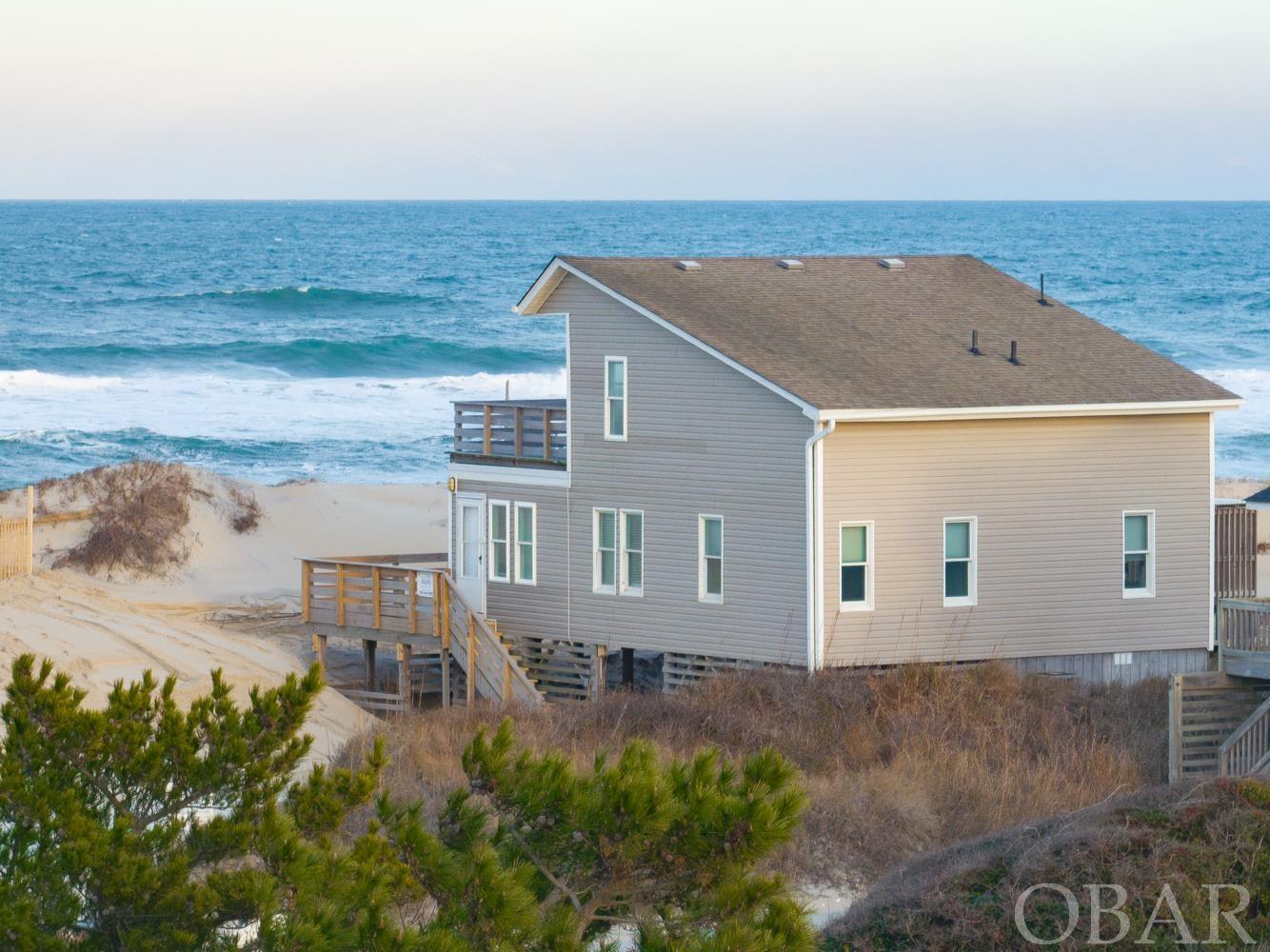 Enjoy everything quaint South Nags Head has to offer in this oceanfront cottage. Located behind a protective dune, this property does not lack views. The first floor includes a spacious living room, dining area, kitchen, two bedrooms, and a hall bath. Upstairs you will find two additional bedrooms, one ensuite, and a private upper deck with panoramic views. This home does not lack outdoor living space with generous decking on the first floor perfect for sharing a meal, just hanging out, or enjoy a refreshing outdoor shower. The home has a great rental history projected to do at or above $80,000 in 2024. Located adjacent to a lifeguard stand in the summer months.