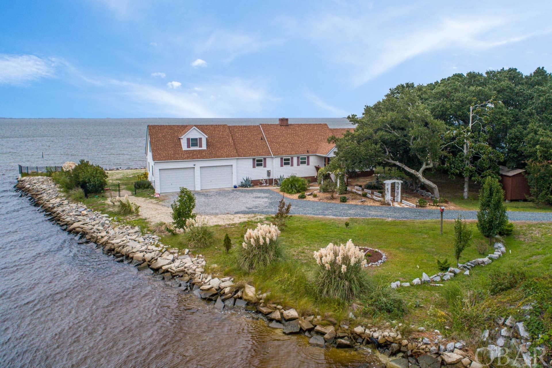 Enjoy serene and sparkling vistas of the Croatan Sound from nearly every room of this exquisite soundfront getaway.  With over 400 feet of unparalleled water frontage, fortified with bulkhead and rip-rap, this residence is a waterfront haven.  Spread across two levels with 5 bedrooms and 4 bathrooms, providing ample space for relaxation and comfort.  Thoughtful and quality features include a custom kitchen with solid wood cabinetry, stainless appliances, a gas cooktop, and separate coffee bar, a large sunroom with UV blocking windows, a 5-person hot tub that overlooks the sound, a first level master with a private deck, and a two-car garage with a back side garage door for yard maintenance.  The upstairs master suite includes a private deck, soaking tub, and tiled shower.  Upstairs you will also find two additional bedrooms and another full bathroom.  Recent updates include, an updated kitchen including a new 6 burner gas cooktop, new kitchen faucet and double wide sink, new designer pendant lighting, a new tile backsplash, new flooring, and new blinds and shades in the kitchen, new interior paint throughout, brand new bulkhead and rip-rap, a new metal ornamental fence, and newly painted decks. Conveniently located in the picturesque town of Manteo, known for its charm and scenic beauty, and just 7 miles to the oceanfront and Jennette’s Pier.  You will spend your summers swimming in the shallow sandy bottom sound, and your winters cozied up by the gas burning fireplace in the heart of the home.  Add this home to your list and see it for yourself!