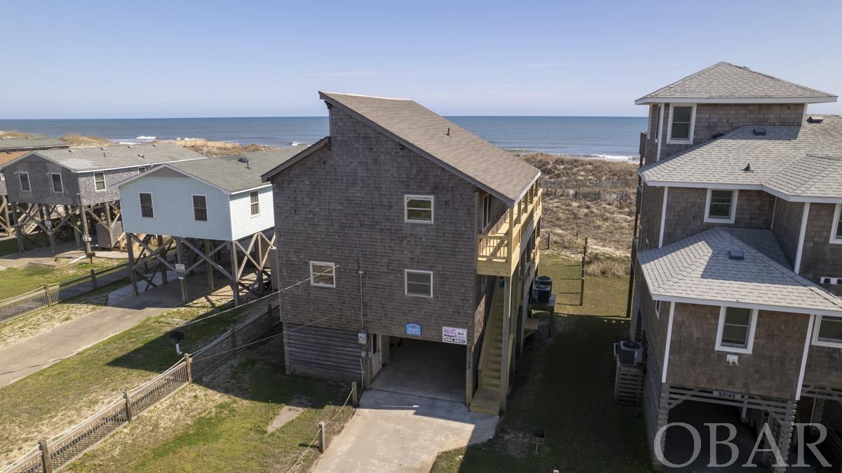 Bring the golf cart and enjoy your summers cruising the village in this well maintained Hatteras oceanfront! The home sits well away from NC 12 Highway which offers less traffic, a peaceful surrounding and excellent views of the ocean tranquility. The ground level area includes a fish cleaning table,  outdoor shower and a large enclosed storage area that is part finished and has a 1/2 bathroom. This storage area is perfect for the beach gear and equipment.   The mid level features 3 bedrooms and 2 full bathrooms with updated LVP flooring, new interior paint and updated bathrooms with tile flooring.  Walking up to the top level you are greeted with soaring ceilings, warm wood walls and all tile floors. The top floor has a dining area, breakfast area and nice size kitchen and living area and a half bathroom. The home has double decks (replaced last year) and fabulous ocean views. If desired, an old survey on file shows where a pool could possibly be situated in the rear yard. Please ask for a full list of updates to appreciate the care and maintenance put into this property and come see this charming Mermaid By The Sea!