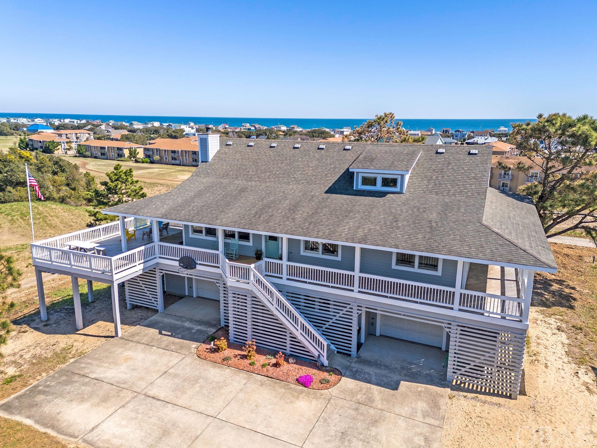 Welcome to your Outer Banks dream beach house! This exceptional home,  thoughtfully designed by the owner, offers many features that set it apart from the competition and has room for a pool.  The first thing to catch your attention is sure to be the impressive high elevation with ocean views from every level.  The floorplan is extremely functional.  As you ascend the stairs to the full wrap-around covered porch you will be drawn to the views of the 18th green of Sea Scape Golf Links to the north and the magnificence of the Atlantic to the east. The very same views are the best feature of the spacious great room area that serves as the heart of the home. The spacious kitchen provides lots of counter space and tons of cabinets for storage with extra seating at the island. On this level you will also find three bedrooms, including a large ensuite with a walk-in closet and, you guessed it, those amazing ocean views. Up one more level you will enter a remarkable bonus room with endless possibilities and more ocean views.  In the lower level of the home you will find many nice surprises including an oversized bedroom that would make the perfect guest room with a full bath just down the hall. The utility room is also located on this level along with a separate workshop and TWO separate full-sized garages. It is built to last with purpose driven attention to detail everywhere you turn, like a generator panel installed, so you can rest easy knowing that your home is prepared for any unexpected power outages. The upgraded Manabloc plumbing system centralizes and organizes the plumbing lines, allowing for easy access and control of the water distribution throughout the property. A  50 gallon Le Bleu water system gives you convenient access to premium drinking water. This location is a rare find with some of the highest elevations around. It offers convenience and a lifestyle like no other. Close to so much including the neighborhood Sandtrap Tavern at the Sea Scape clubhouse.  The beach and some of the best local food and beverage establishments on the OBX are within walking/biking distance. This one has to be seen to be appreciated. Don't miss the virtual tour link. Want to add a pool? The Seller has preliminary approval from the town to add a 9'1" x 17'5" pool.