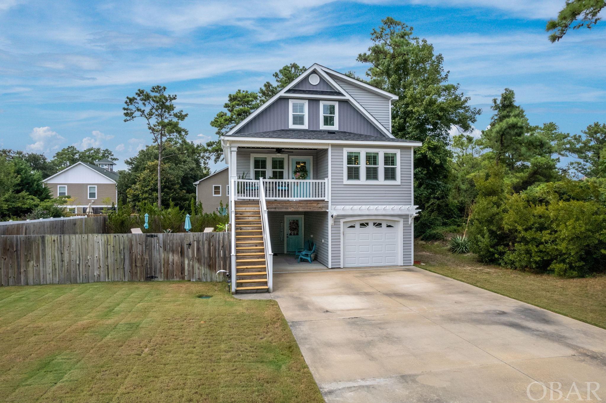 This modern, stylishly upscaled 4-bed, 3.5 bath saltbox is downright immaculate and is quite simply gonna knock your socks off! It's location just can't be beat - in the heart of Kill Devil Hills on a corner lot in an established westside neighborhood. You're close to, well, just about everything the Outer Banks is known for, and most within walking distance - great restaurants, shopping opportunites and attractions, even the maritime forests of Nags Heads Woods Preserve! Let's start with the outdoor living here. It's off the charts! In-ground gunnite saltwater pool, hot tub w/sound system on paver patio shaded by a pergola, covered tiki bar with lots of seating and sun-drenched patio seating, all near the pool. Plus, it's all surrounded by a privacy fence bordered with lush landscaping and plenty of yard. You and your guests will have a blast! Entering the home from the covered patio/tiki bar, you're welcomed by an inviting functional mudroom with a sitting bench and plenty of storage options. On this floor, you'll also find a spacious bedroom (owners are uitilizing as an office) en-suite with double sinks and storage built-ins. The attached one-car garage is tiled and has built-in cabinets to store all your pool and beach accessories. As you move up to the main level of the house, it just keeps getting better! Beautiful hardwood floors and custom plantation shutters frame the open-concept living area lending a cozy, but distinctive airiness combined with the soaring cathedral ceilings. The stylish kitchen with  generous-sized prep island, stainless steel appliances, smooth quartz countertops, large apron-front stainless sink, pantry and gorgeous tiled backsplash will satisfy even the most discerning of chefs and is completely open to the adjacent dining room. Down the hall is a serene master en-suite, complete with double sinks, custom-tiled shower, built-in open shelving and access to a walk-in closet and very functional laundry room with storage cabinets and hanging rod. On the top level are two more spacious bedrooms flanking a full-sized Jack-and-Jill bath, all beautifully updated. This home is truly amazing and absolutely turn-key! Don't miss out! Book your showing today!