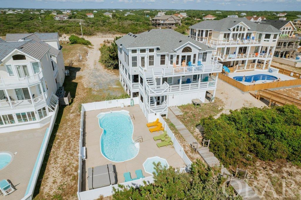 EXQUISITE "LUXURY" BEACH LIVING. This "WELL MAINTAINED" stunning home is topped off with the most magnificent Sunrise views of the Atlantic Ocean and Sunset views over the Currituck Sound. Located on the ever sought after 4X4 Beaches of Corolla, also home to the Majestic "Wild Ponies" and numerous other species of wildlife.     Enjoy gorgeous panoramic ocean views and watch the dolphins play or sit on the large, covered side deck while enjoying your coffee, a hammock and near daily visits from the wild horses. The beach is a short walk over the dunes on your private walkway that was completely rebuilt in 2021. The top floor of this open reverse floor plan has a large, open great room along with a powder room and 2 master suites and a deck running the full east side of the house to enjoy the sunrise. The second floor holds four master suites with renovated bathrooms and a large, covered side deck as well as a beach facing deck running the length of the house. The ground level has two bunk bedrooms with a large jack and jill bath, powder room, laundry room and second entertaining area with a kitchenette. This second living space is great for the kids to play video games or hang out while the adults have their own gathering space on the top floor.  In addition to enjoying the beach just steps away, this home boasts a private pool and newer (2020) hot tub. There is even a shallow kiddie pool built into the pool deck! The pool area is to the south of the house. Adjacent to the pool there is a lavatory, a shower and a beach toy storage room.   With many improvements since 2020, including new siding, new roof, a new well, fresh interior paint, and 2 of 3 HVAC units replaced, this well-maintained home is ready for you to enjoy along with your friends and family or keep it in a rental program for great ROI. LOCATED IN AN "X" FLOOD ZONE...WHICH MEANS...NO FLOOD INSURANCE REQUIRED!!!