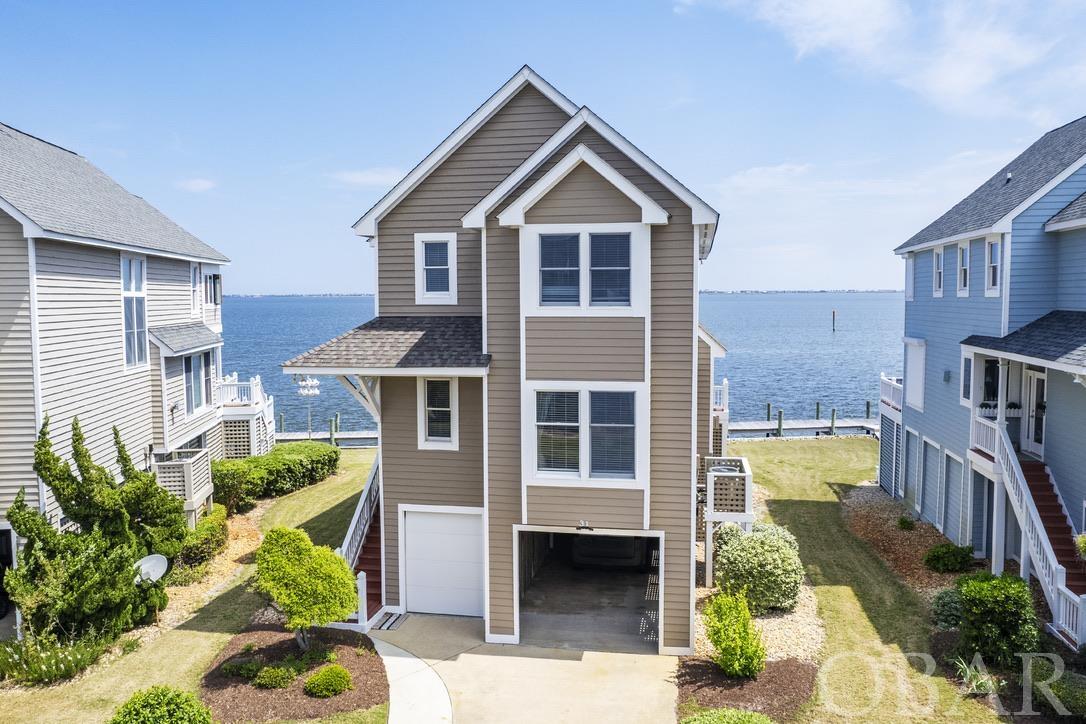 Located on the soundfront, close to great fishing, boating and of course our world famous Outer Banks beaches, this 4 bedroom 3 bathroom home in the Pirate's Cove community is turn-key AND comes with it's own boat slip assignment. The sweeping sound views greet you as you walk thru the door into the open concept living and dining space. Enjoy waterfront dining in your own home. The kitchen features granite countertops, stainless steel appliances, farmhouse sink and pantry. Cozy up to the gas fireplace in the fall and winter, and enjoy the water views all year. A porch spans the entire east facing side of this level, with a sunken hot tub on one side. It's a great spot to relax after a long fun day on the beach or on the water. Enjoy the shade under the covered portion of the porch, or step out into the sunshine, it's your choice, you have both options! This level of the home also features a bedroom with en suite bathroom and laundry space. Walk up the stairs to another large bedroom with its own private soundfront covered porch, en suite bathroom and fantastic water views. There are two other bedrooms on this level, as well as a jack and jill bathroom. Every room comes fully furnished and decorated in a coastal and fishing inspired theme. The ground level features a large conditioned storage space. Some owners opt to park a golf cart in this space, and still have plenty of room for beach toys and fishing gear. An outdoor shower and stainless steel fish cleaning table with sink round out the ground level in this waterman/waterwomans ideal property. AND this home comes with it's own 25' boat slip assignment. It's steps away, on the canal side, keeping your vessel more protected from the wind. The Pirate's Cove community is centrally located between Nags Head and the town of Manteo, in very close proximity to the Oregon Inlet Marina and fishing center and features a marina, restaurant, tiki bar, multiple pools, fitness center, tennis and playground. It's a popular choice for boaters and fishing enthusiasts and hosts multiple fishing tournaments and events throughout the year, that bring owners and guests together to enjoy the fruits of our waters. Beachgoers love the ease of access to the ocean, while living in a well maintained community with amenities. This section of Pirate's Cove includes landscaping, so you dont have to do anything, just enjoy the Outer Banks. Come tour this fantastic waterfront home and enjoy all the Outer Banks has to offer. Use it for yourself or as a rental income producing investment or both! New roof, carpet and paint inside and outside in 2022.